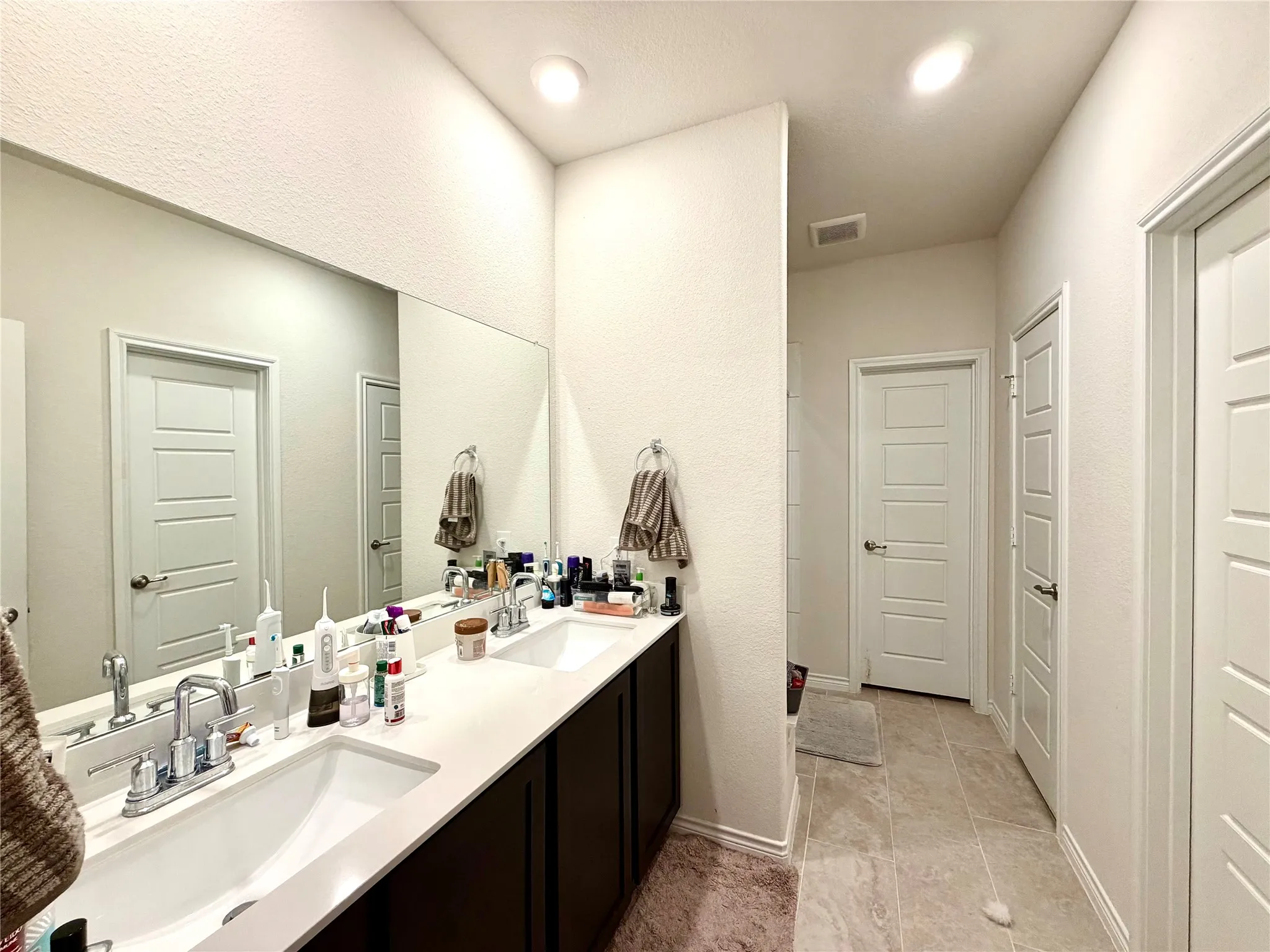 Dual vanity with integrated sinks, expansive wall-mounted mirror, recessed lighting, and tile flooring