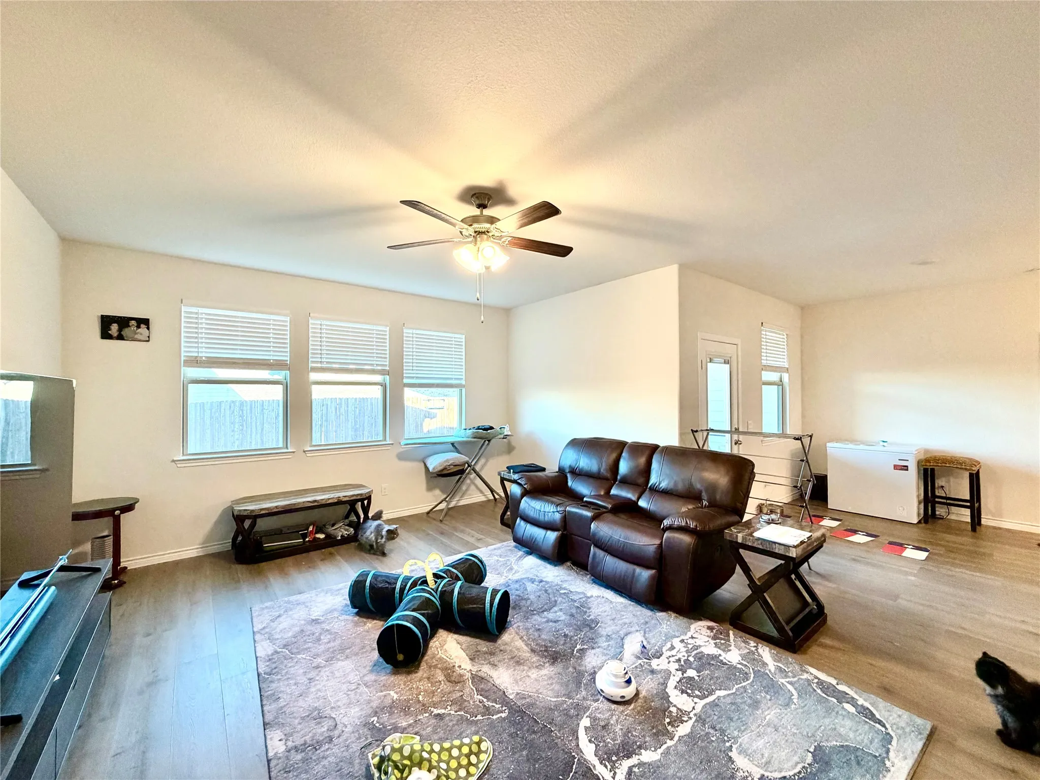Spacious living area featuring wood-finish flooring, a ceiling fan, and multiple windows with blinds