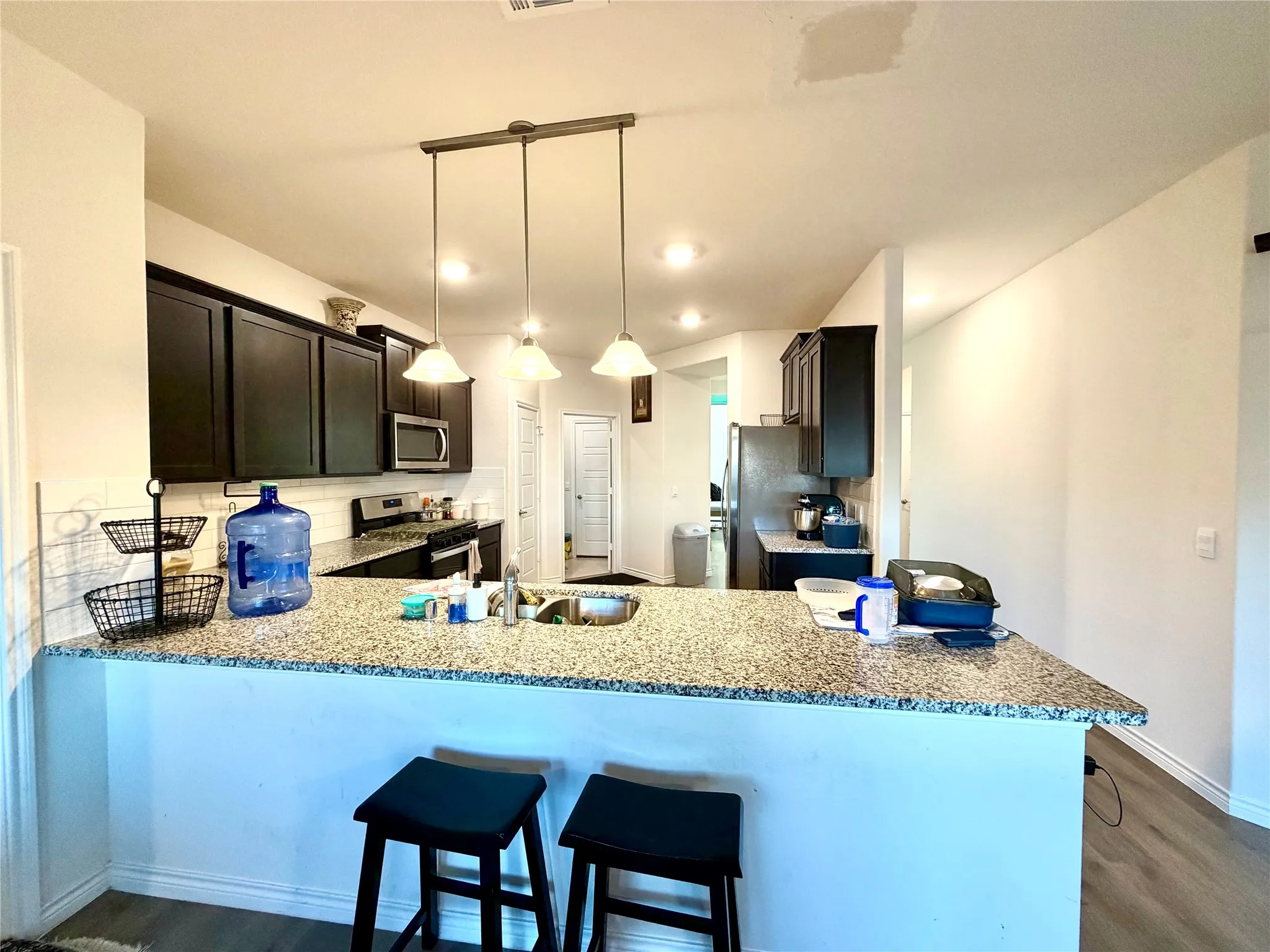 Kitchen featuring dark wood-finish cabinetry, granite-style countertops, stainless steel appliances, and recessed lighting
