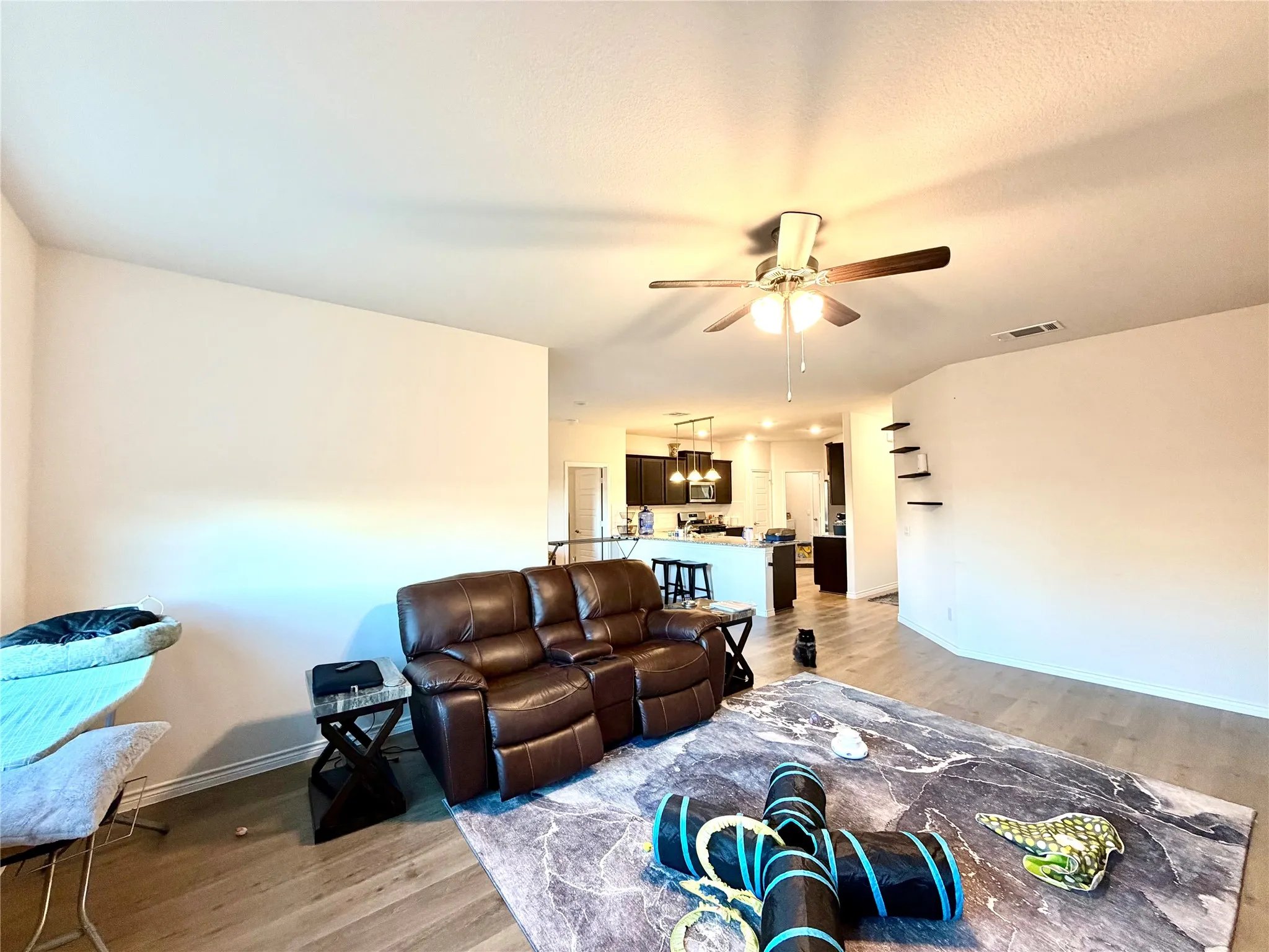 Open-concept living space with wood-finish flooring, a ceiling fan with integrated lighting, and built-in shelving