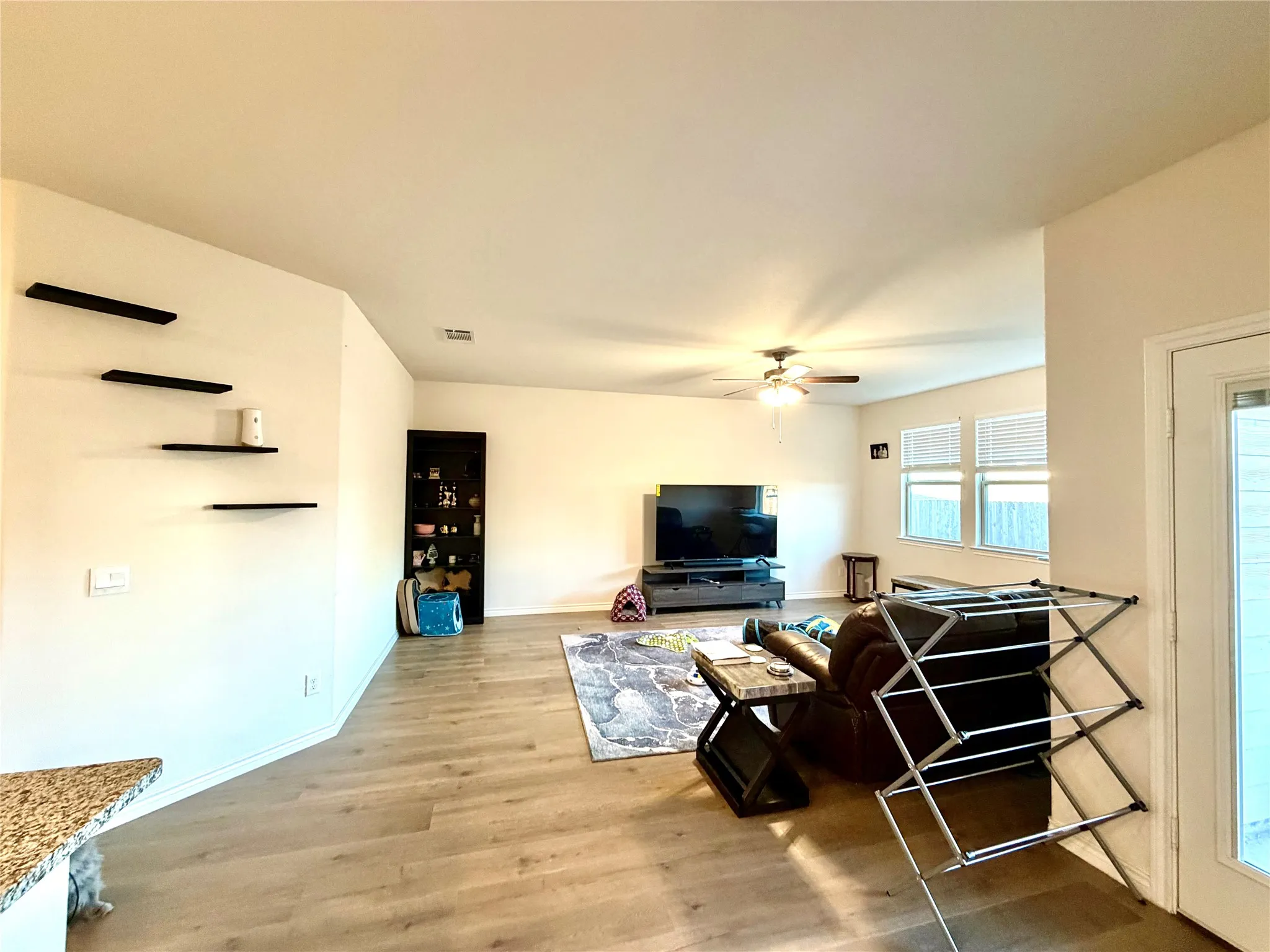 Spacious interior featuring wood-finish flooring, a ceiling fan with integrated lighting, and multiple windows with blinds