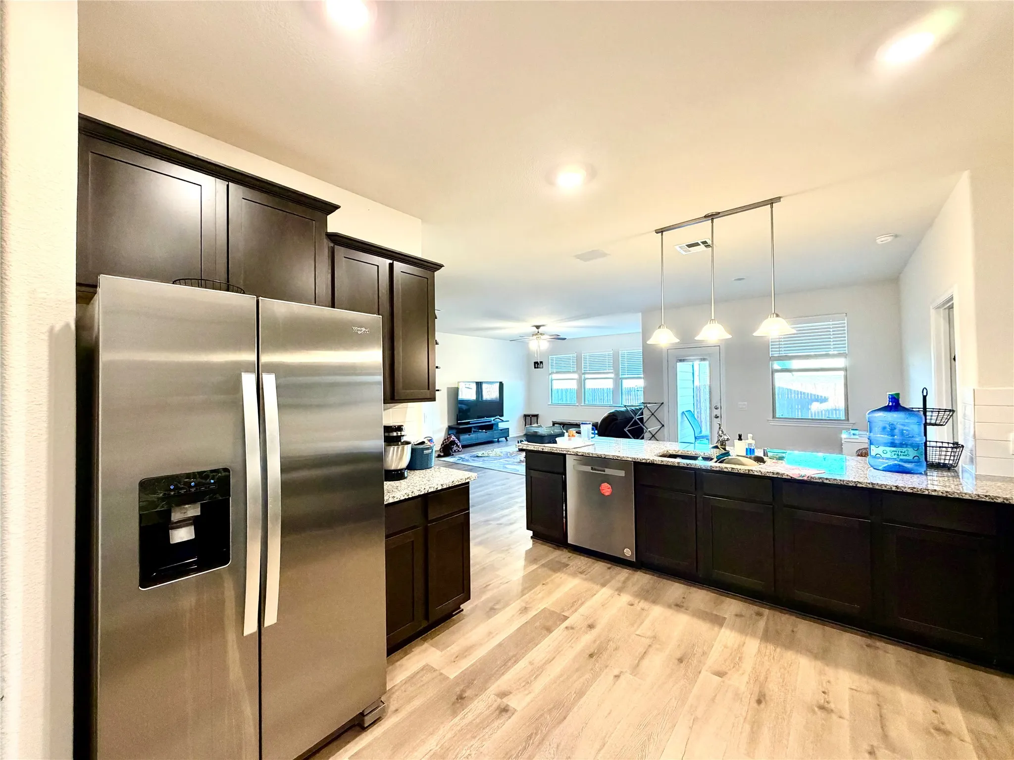 Modern kitchen featuring dark cabinetry, stainless steel appliances, light-toned wood-finish flooring, and a spacious island with pendant lighting
