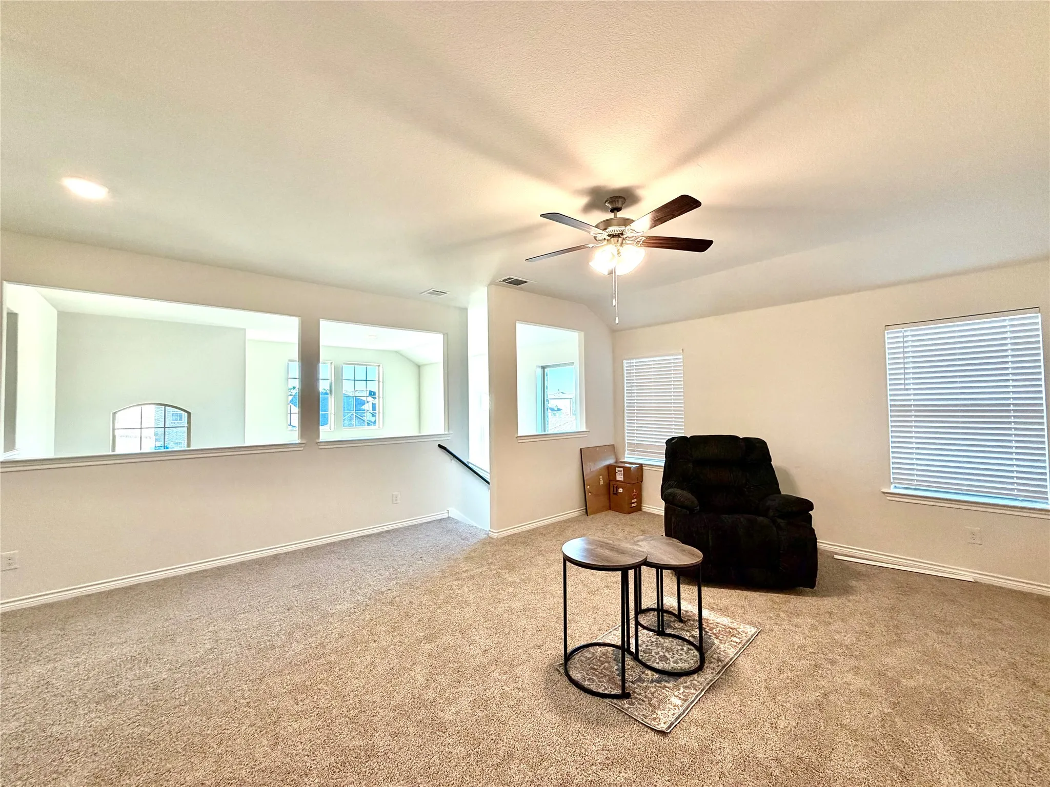 Open concept loft area featuring neutral carpeting, white walls, and a ceiling fan with integrated lighting