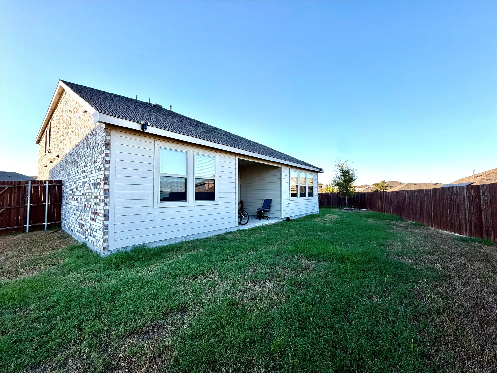 Expansive backyard with a covered patio, privacy fencing, and a combination of brick and siding exterior