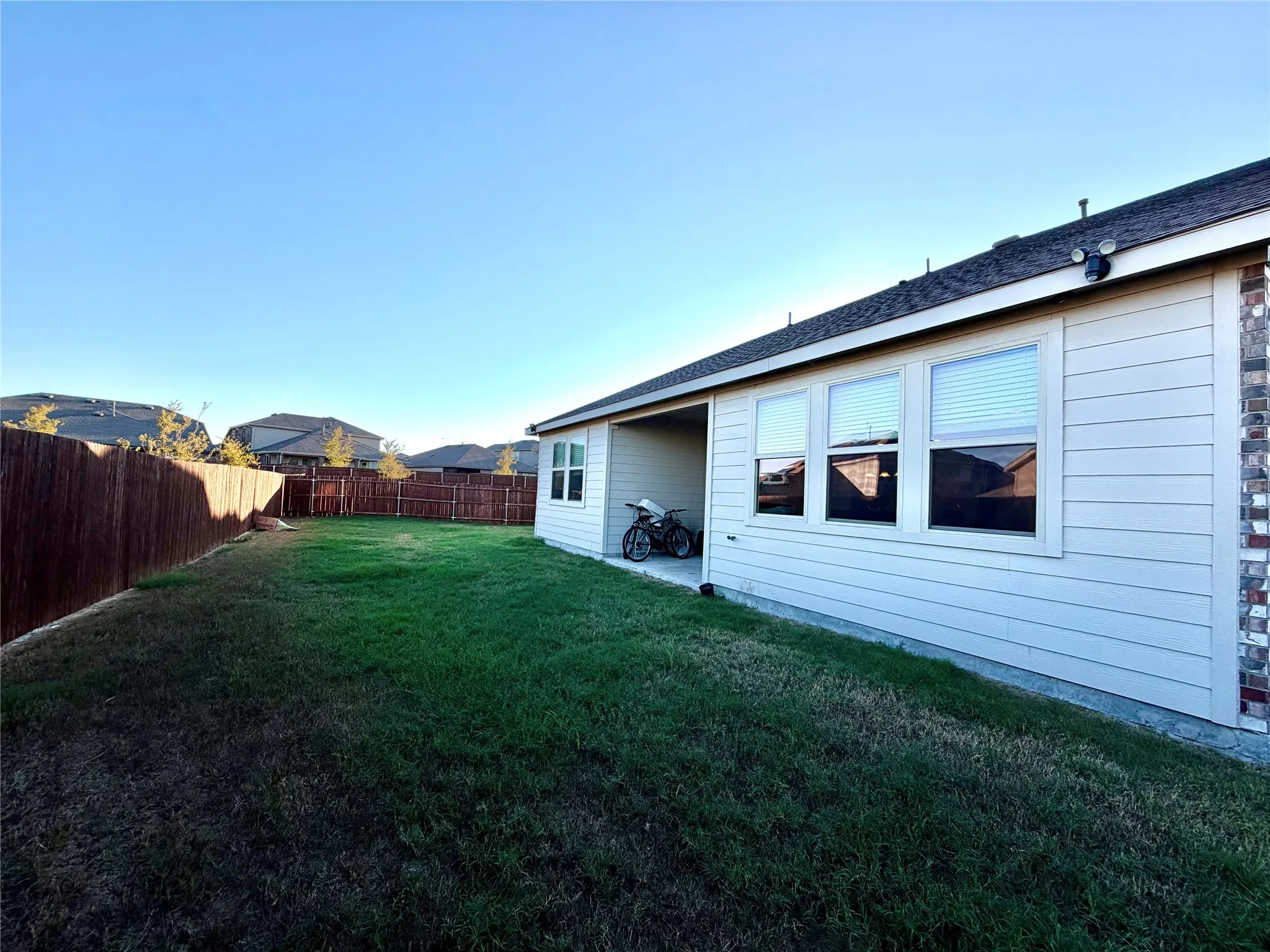 Expansive backyard featuring a manicured lawn, full privacy fencing, a covered patio, and brick exterior accents