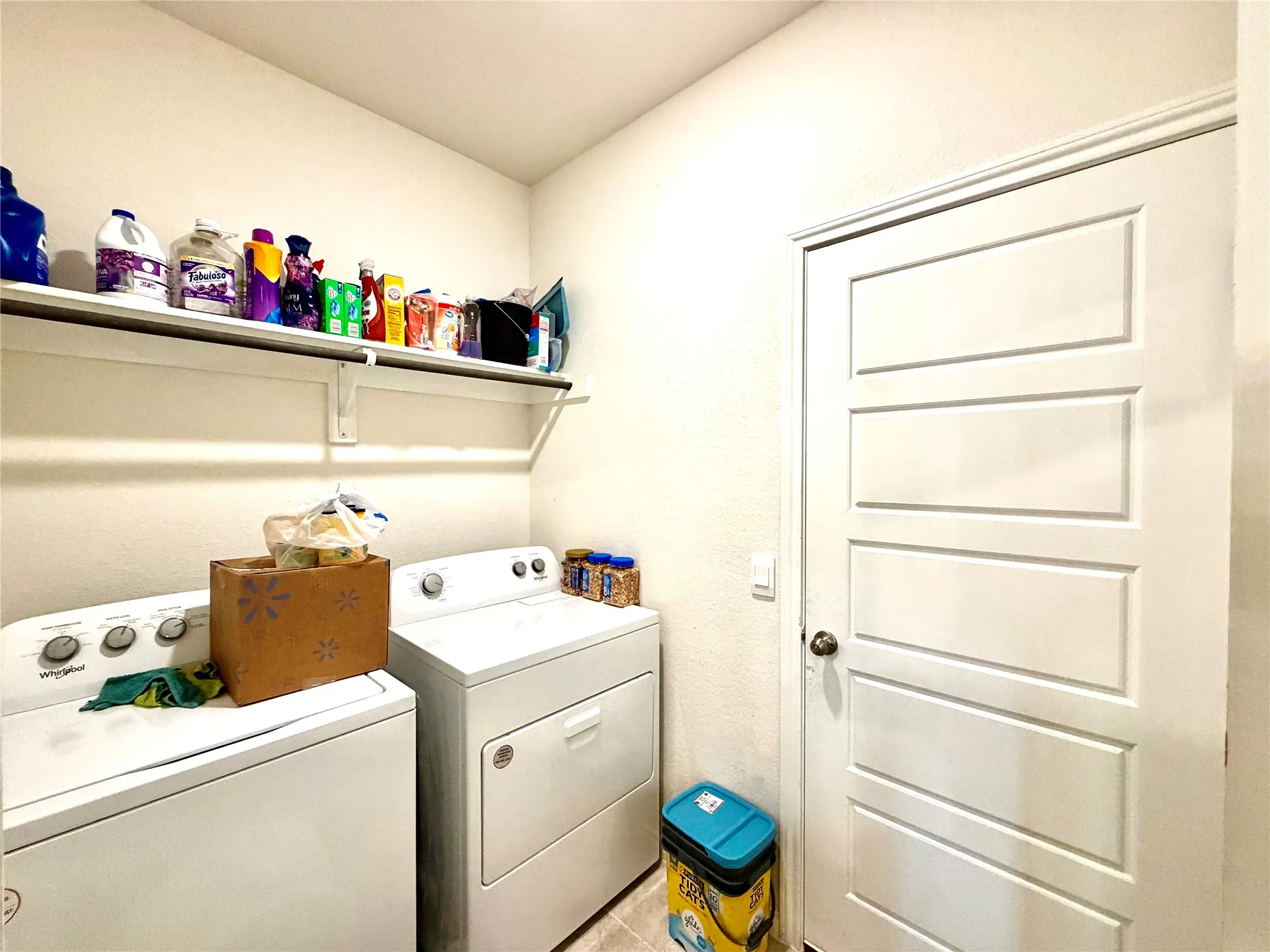 Laundry area featuring an overhead shelf, a white paneled door, and neutral wall tones