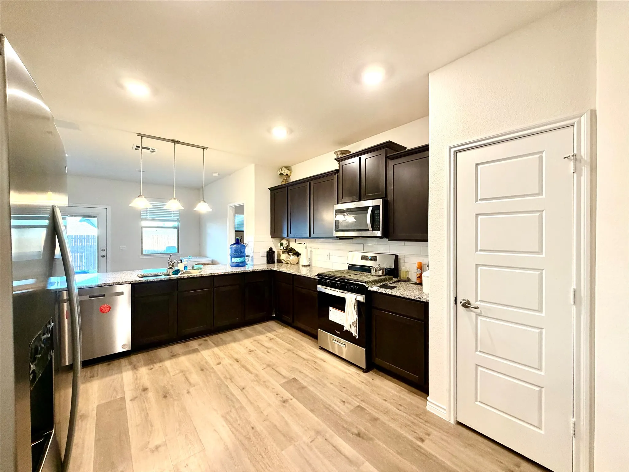 Kitchen featuring wood-finish flooring, dark wood cabinetry, stainless steel appliances, and a white subway tile backsplash