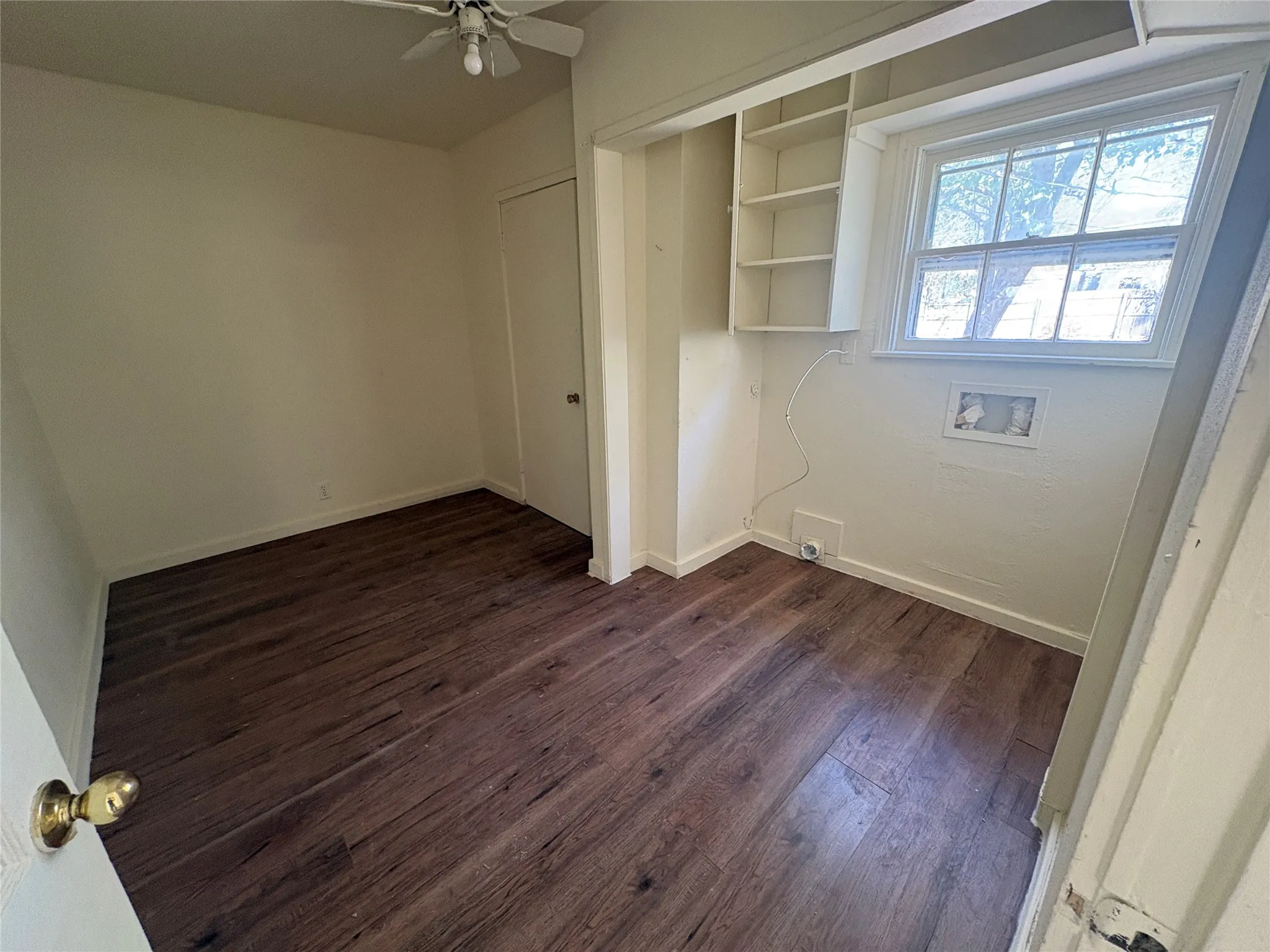 Wood-finish flooring, built-in shelving, ceiling fan, and a window providing natural illumination