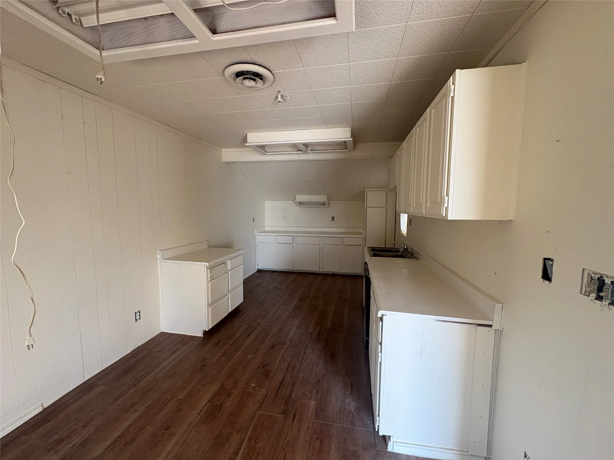 Wood-finish flooring, white cabinetry, white countertops, built-in sink, and drop ceiling