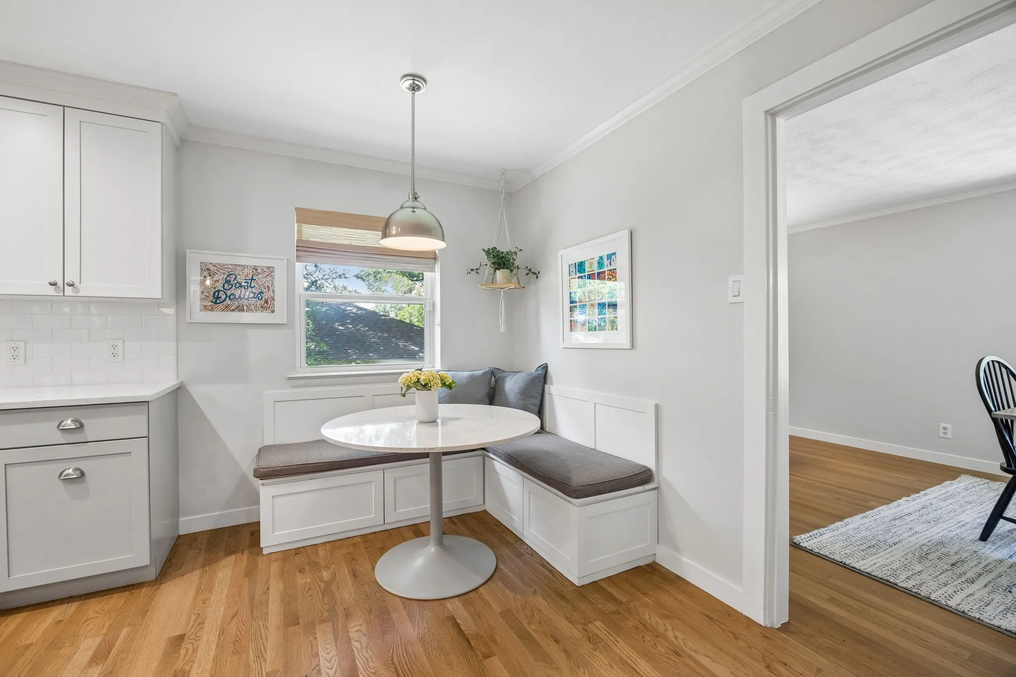 Light wood-finish flooring with white built-in banquette seating, white shaker-style cabinetry, white subway tile backsplash, and a polished chrome pendant light fixture