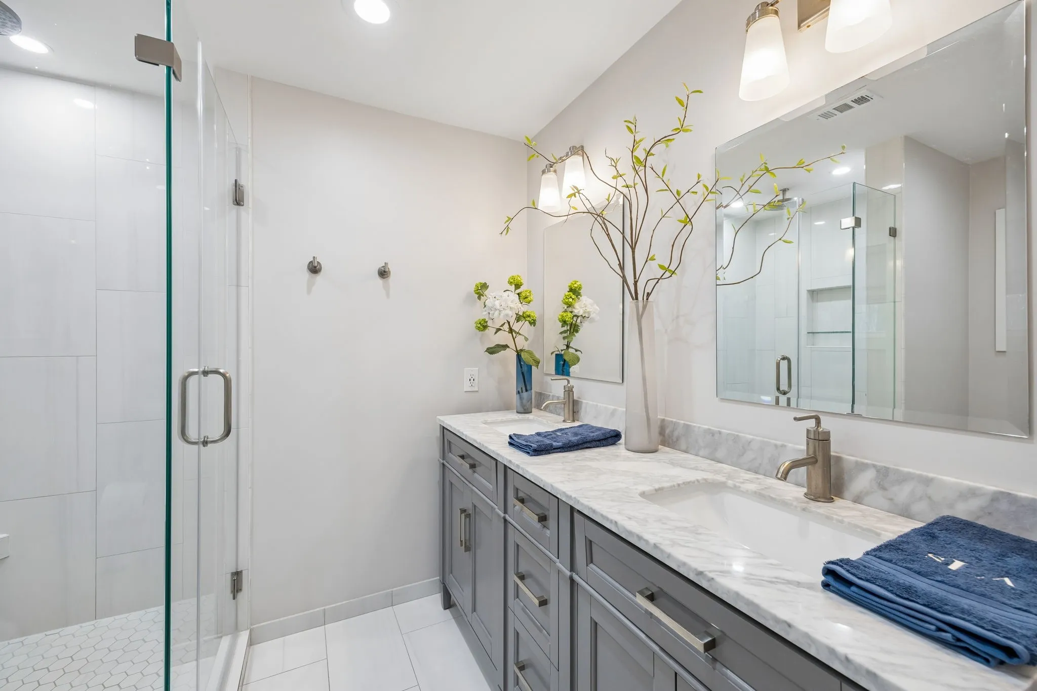 Double vanity with integrated sinks, brushed nickel fixtures, gray cabinetry with modern hardware, marble-look countertop, and a glass-enclosed shower