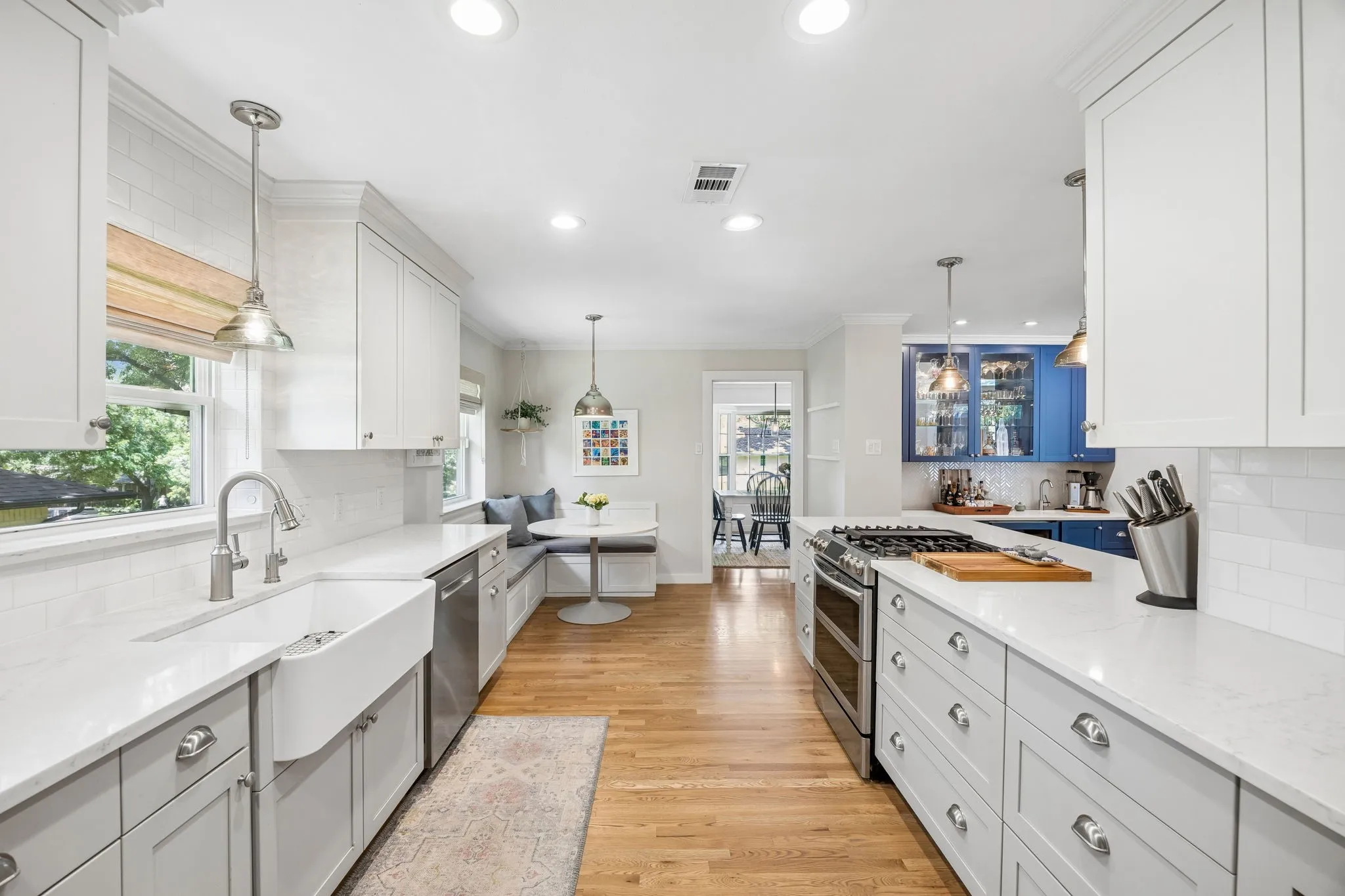 Open-concept kitchen featuring wood-finish flooring, white subway tile backsplash, white and gray cabinetry, and a built-in banquette with a round table
