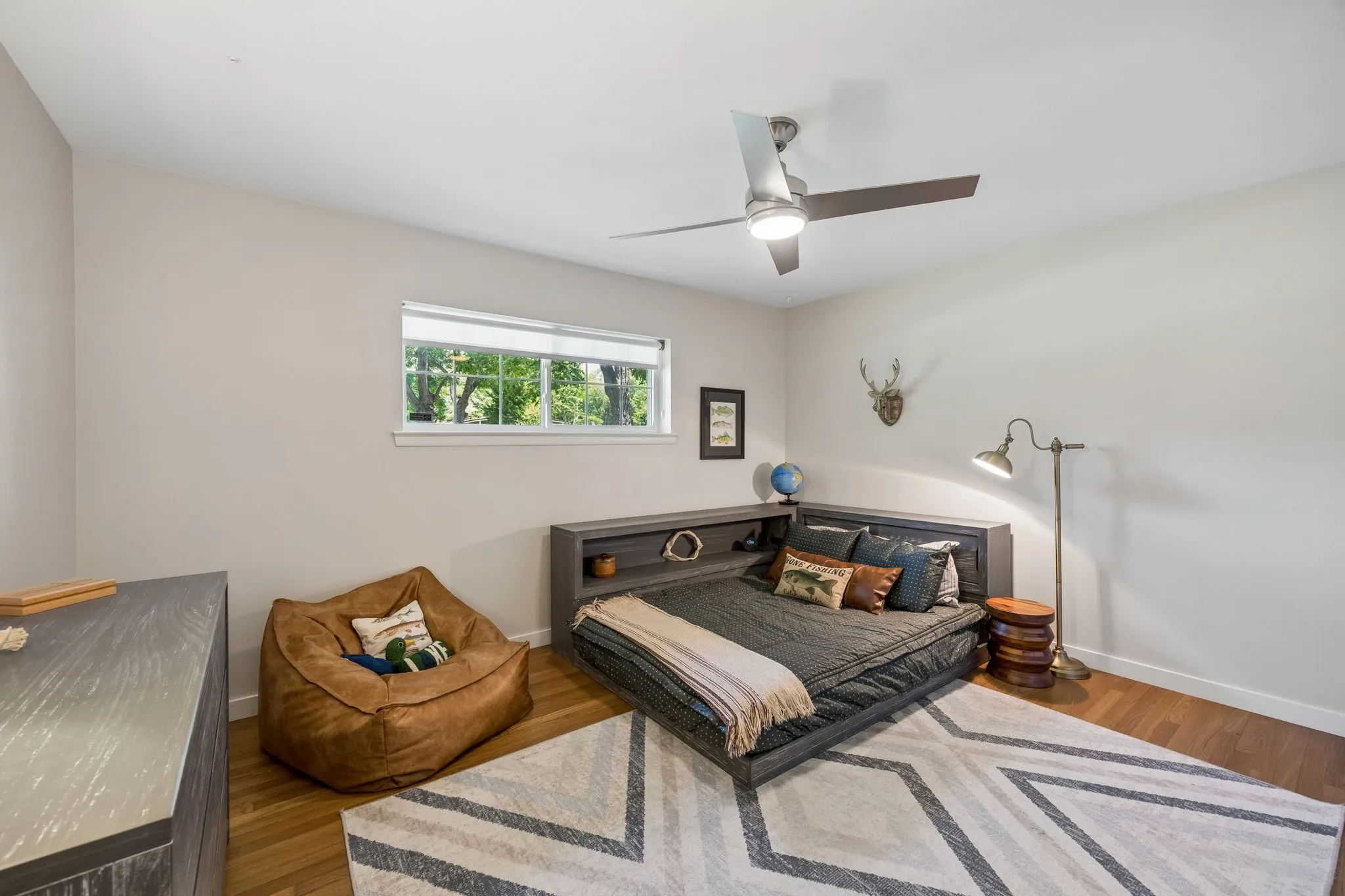 Hardwood flooring, neutral wall tones, modern ceiling fan, built-in shelving, and a bright window
