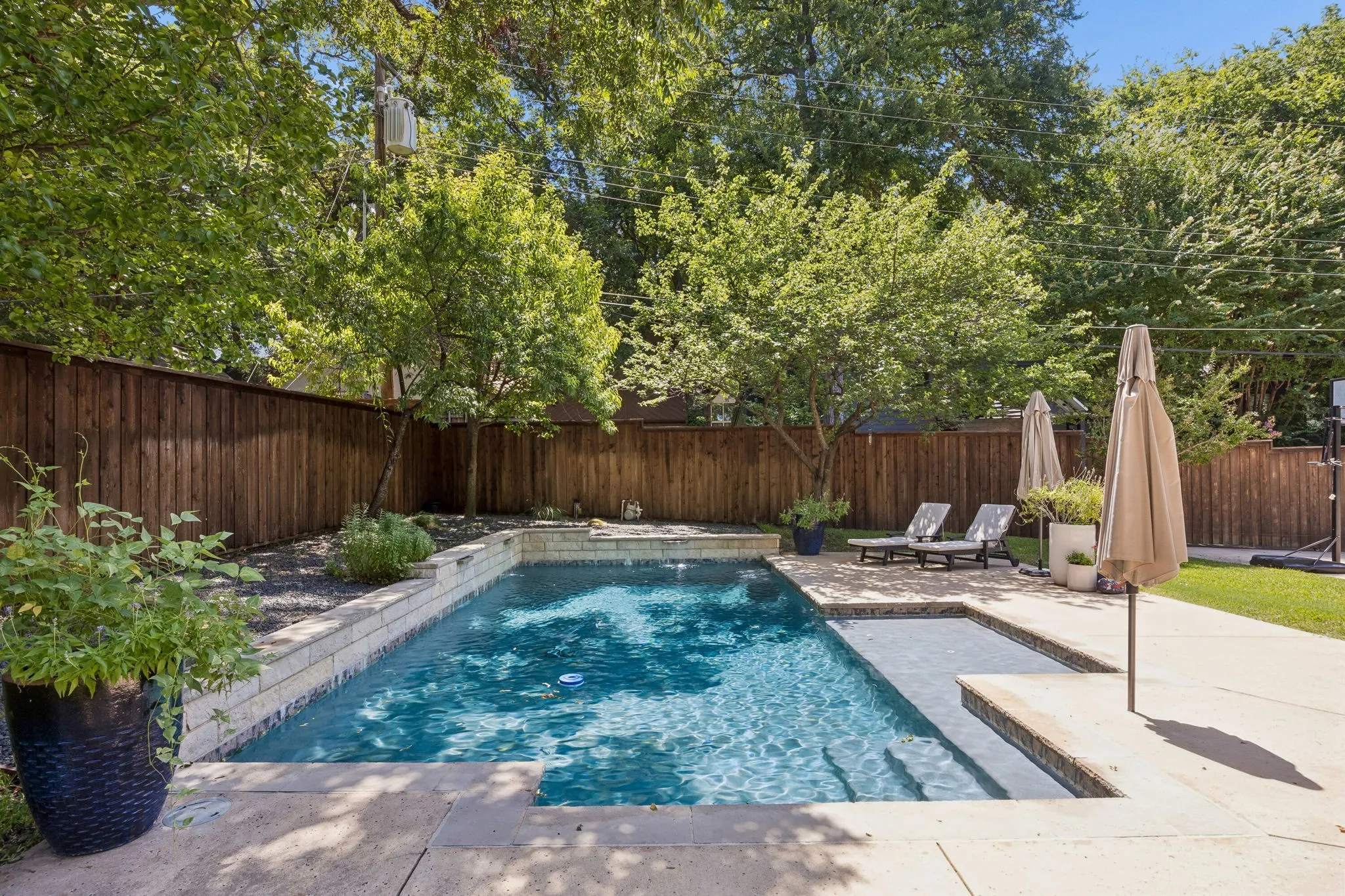 Private backyard featuring a swimming pool with integrated steps, concrete surround, and a wooden privacy fence