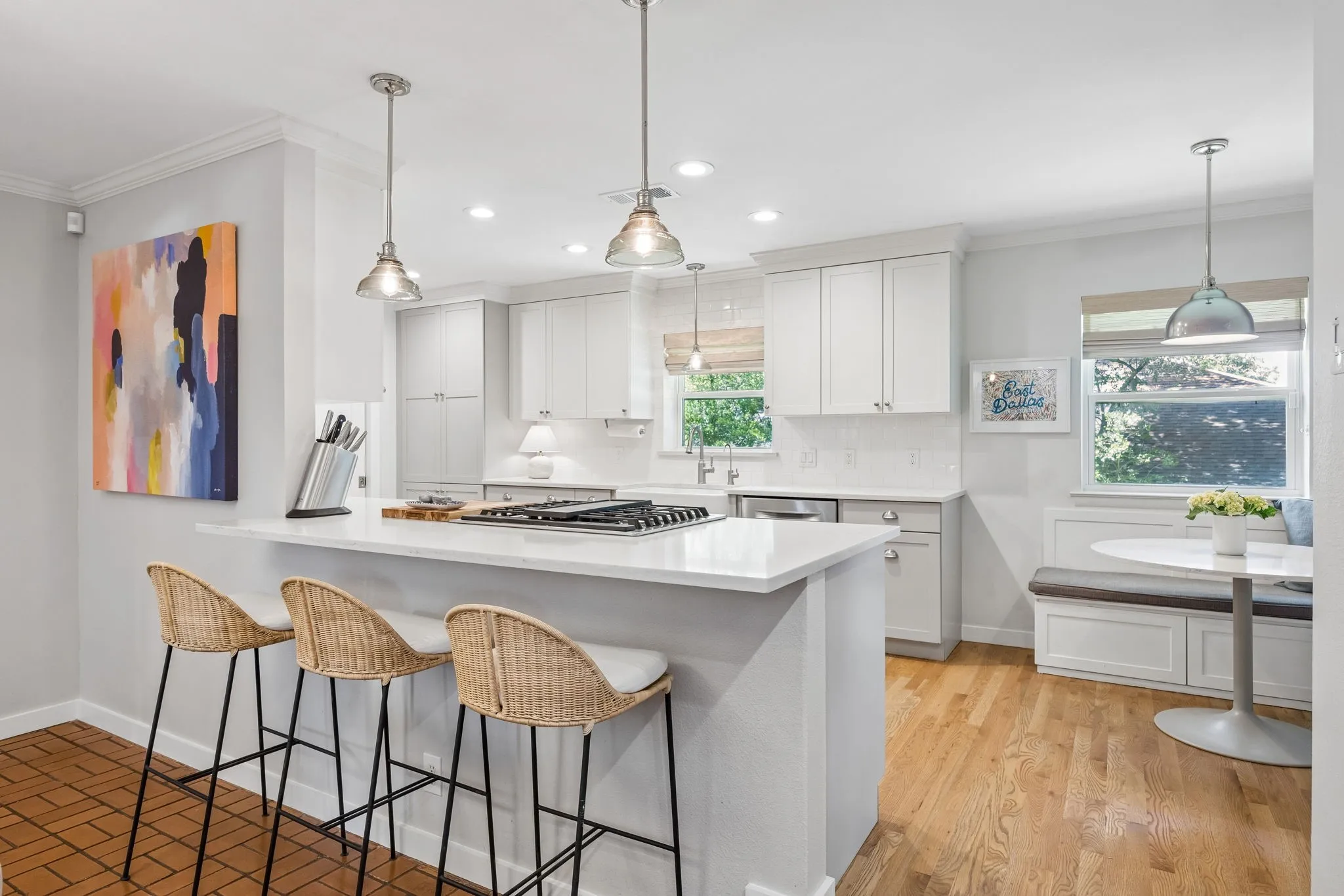 White shaker-style cabinetry, light wood-finish flooring, white countertop surfaces, and a built-in banquette seating area