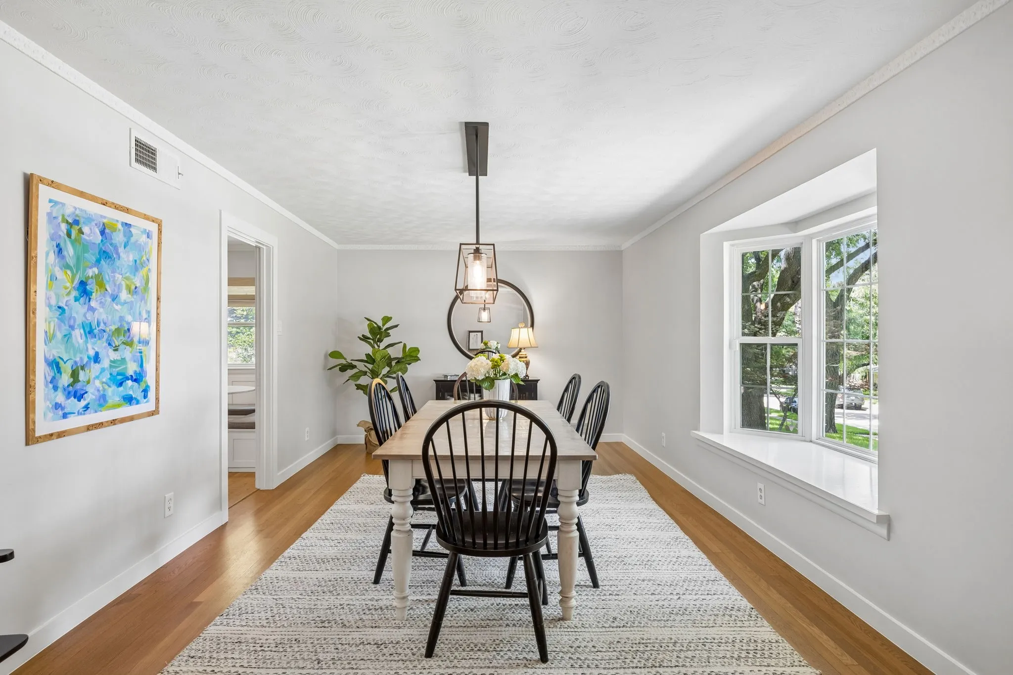 Wood-finish flooring, bay window, crown molding, and a modern rectangular chandelier