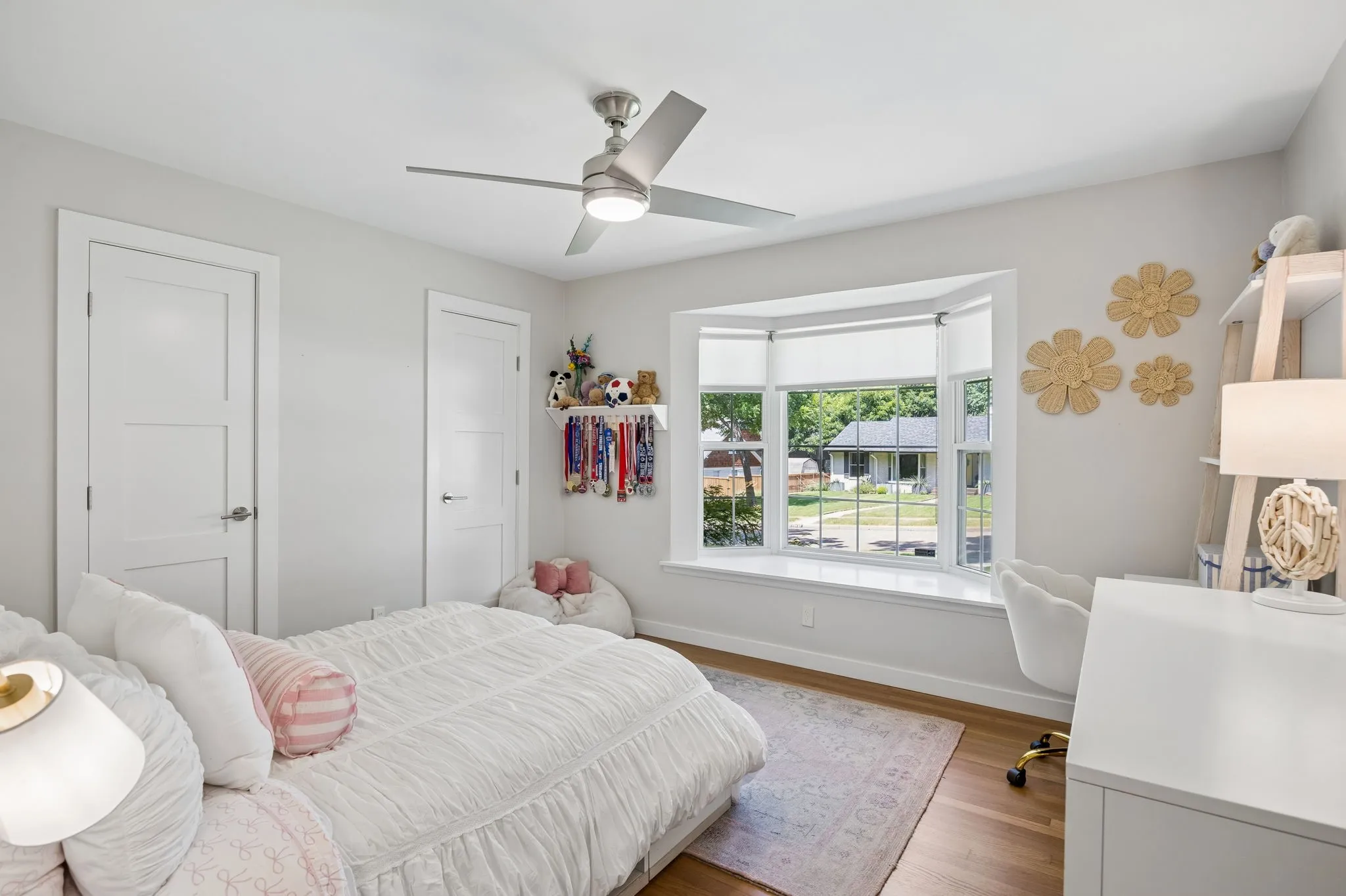 Hardwood flooring, bay window with integrated sill, contemporary ceiling fan, and white three-panel interior doors