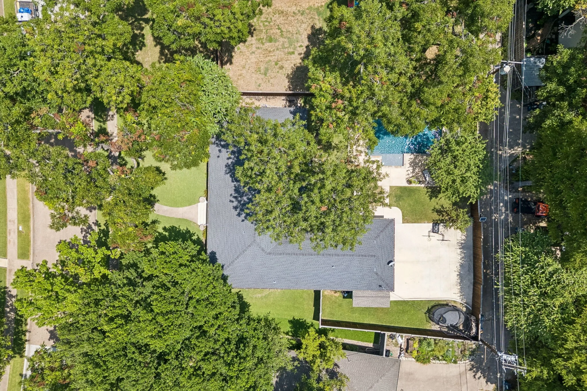 Expansive property featuring a grey shingle roof, large concrete patio, and a swimming pool
