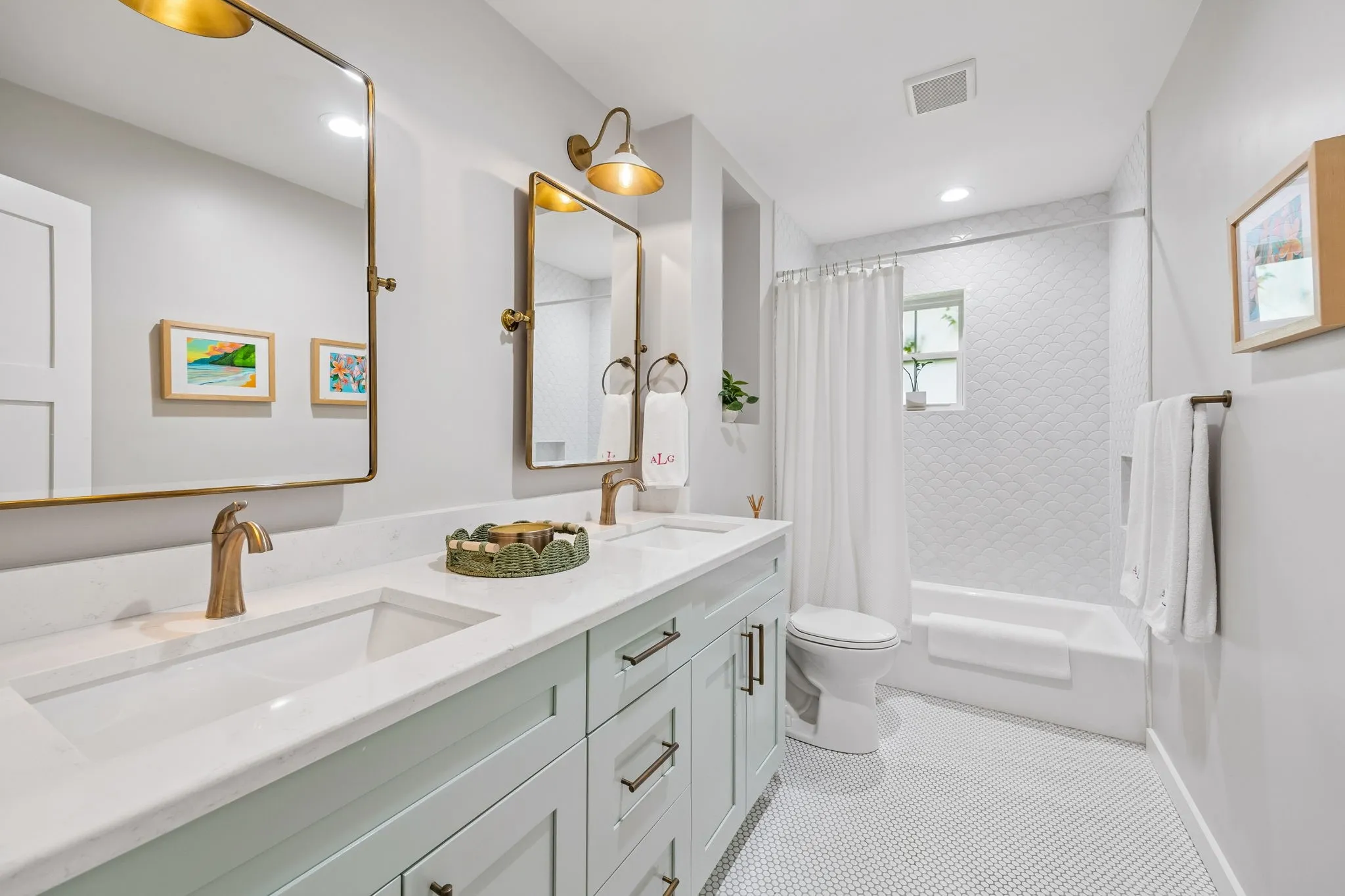 Dual sink vanity with light-toned cabinetry and integrated sinks, brushed gold-tone fixtures, and white tile flooring