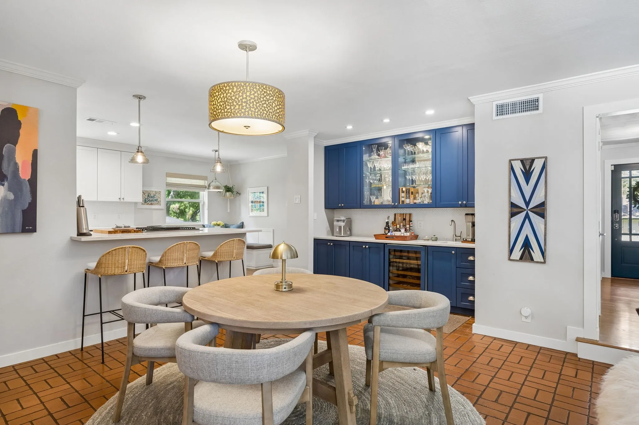 Dining area featuring terracotta tile flooring, a built-in wet bar with blue cabinetry and glass-front upper cabinets, and a kitchen pass-through with pendant lighting
