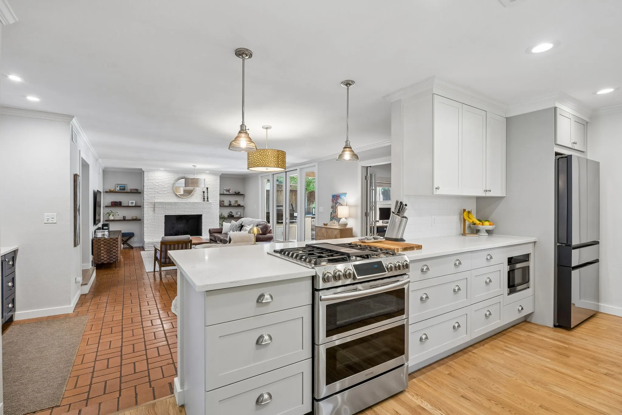 Stainless steel range with double ovens, white cabinetry, integrated microwave, wood-finish flooring, and brick-patterned flooring