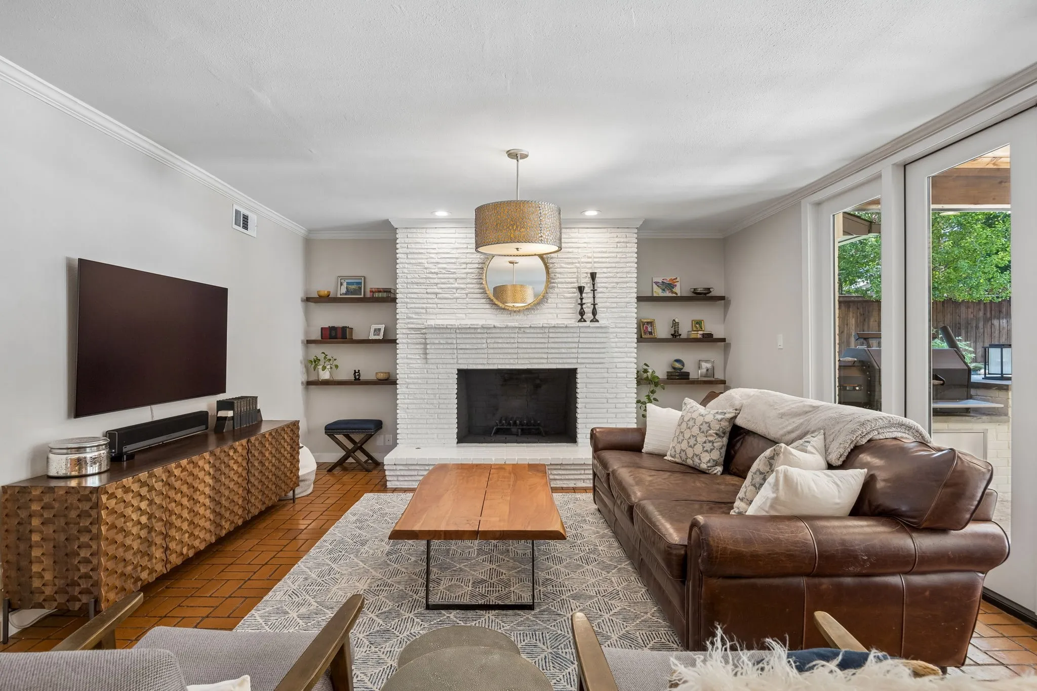 Whitewashed brick fireplace with a hearth, custom floating shelves, wood-finish flooring, and French doors leading to an exterior area