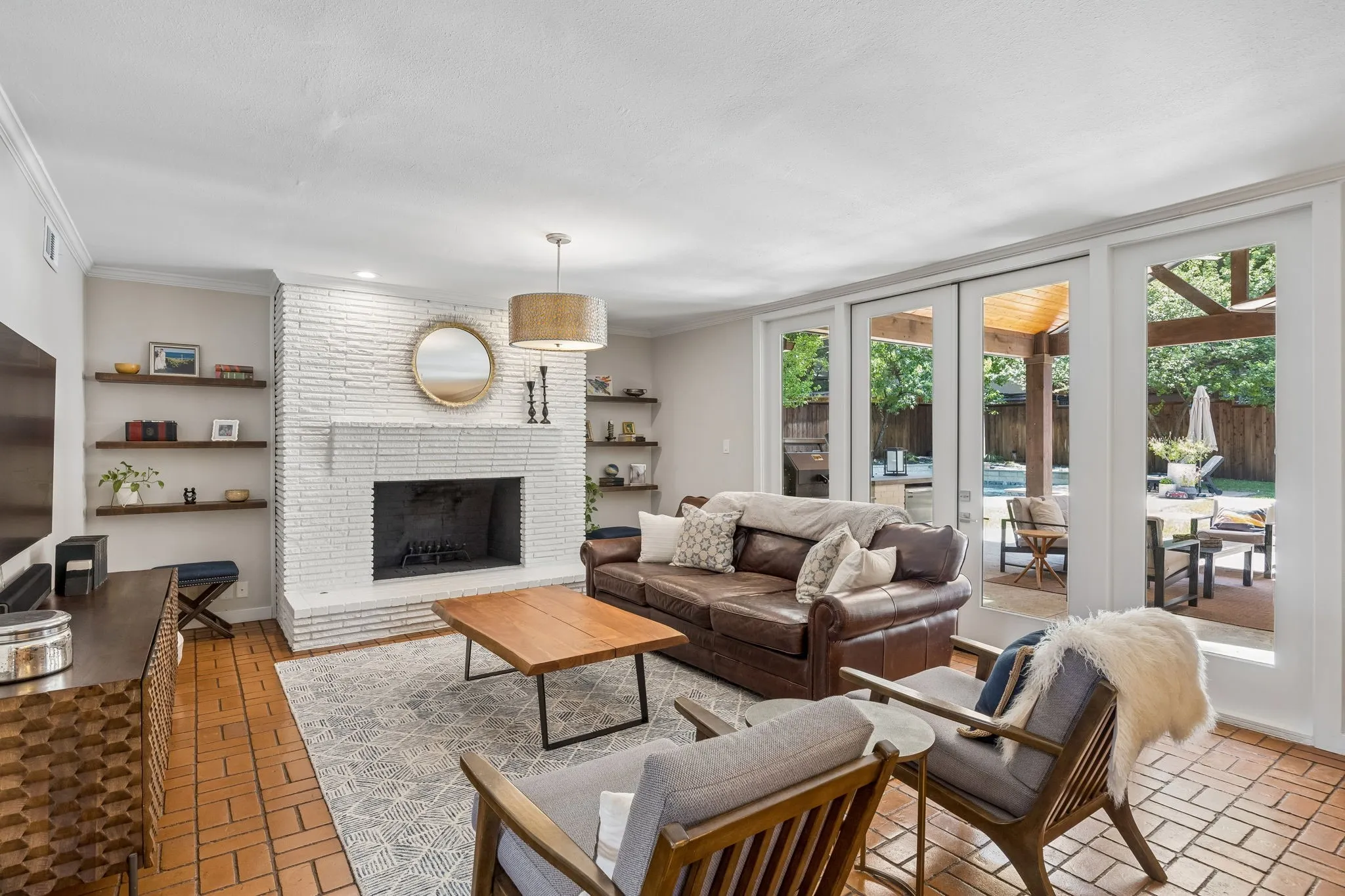 White brick fireplace with hearth, wood-finish floating shelves, terracotta tile flooring, and sliding glass panel doors