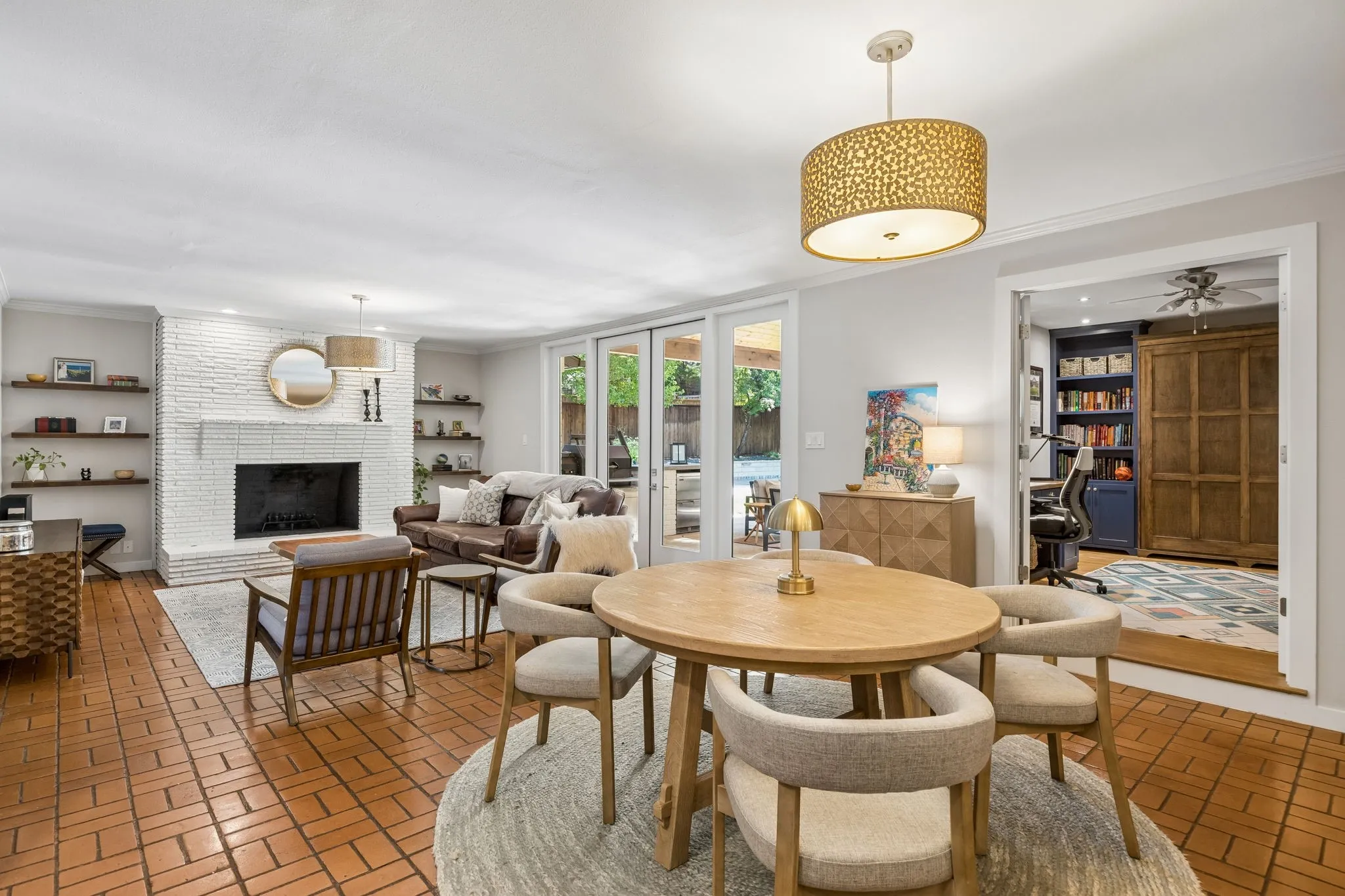 Brick flooring, white brick fireplace, built-in shelving, French doors, and a decorative pendant light fixture
