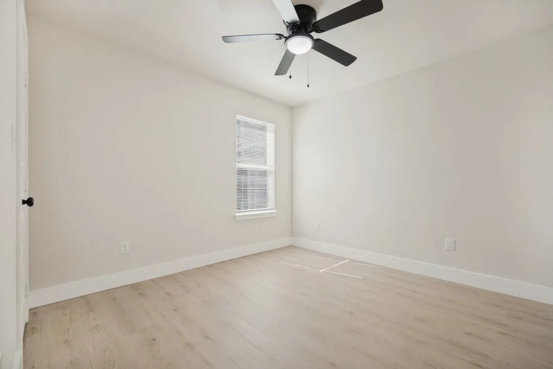 Light-toned wood-finish flooring with white baseboards, a window with horizontal blinds, and a ceiling fan with integrated lighting