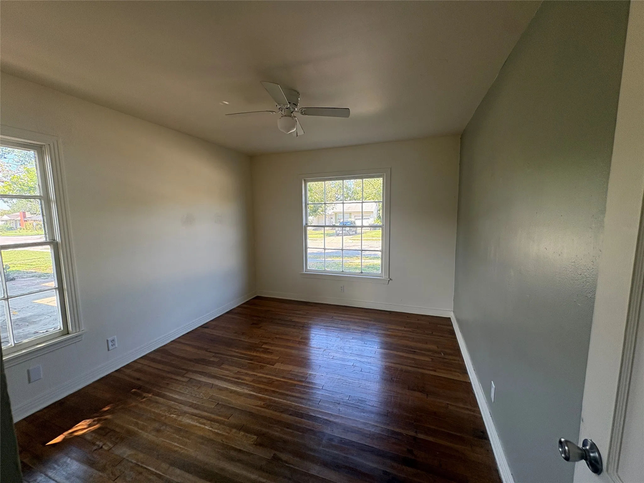 Wood-finish flooring, white trim, multiple windows, and a ceiling fan