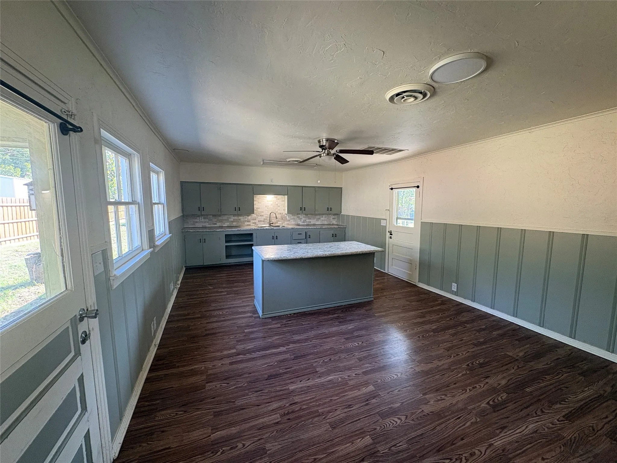 Open-concept room featuring wood-finish flooring, wainscoting, and a kitchen area with an island