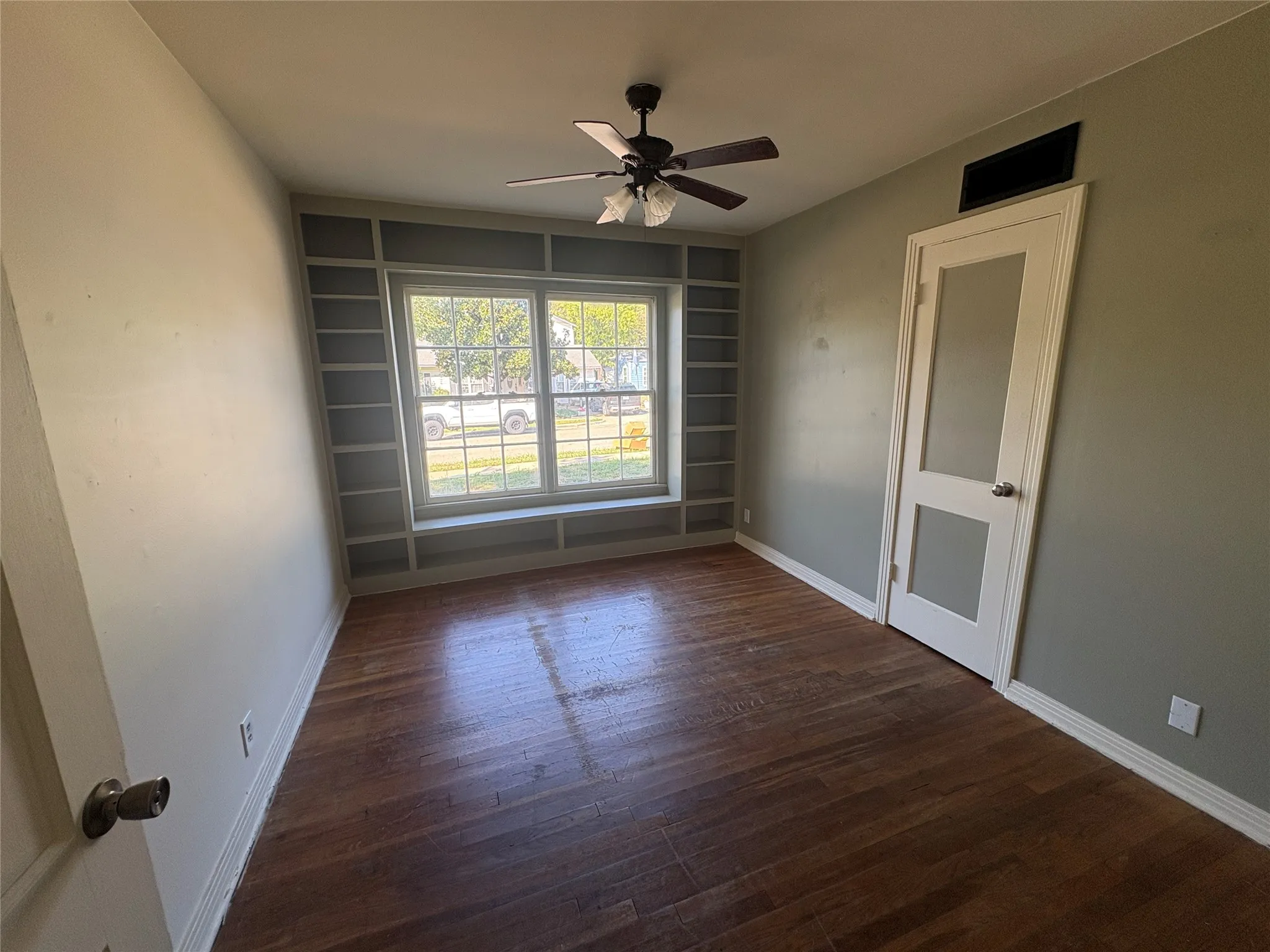 Built-in shelving surrounding a double window, wood-finish flooring, and a ceiling fan with integrated lighting