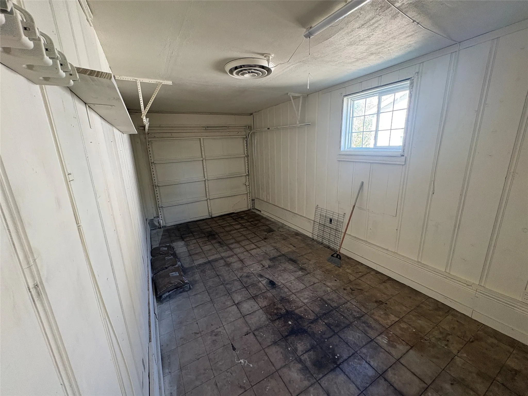 Garage space featuring a paneled wall finish, a window, a single garage door, built-in shelving, and overhead fluorescent lighting