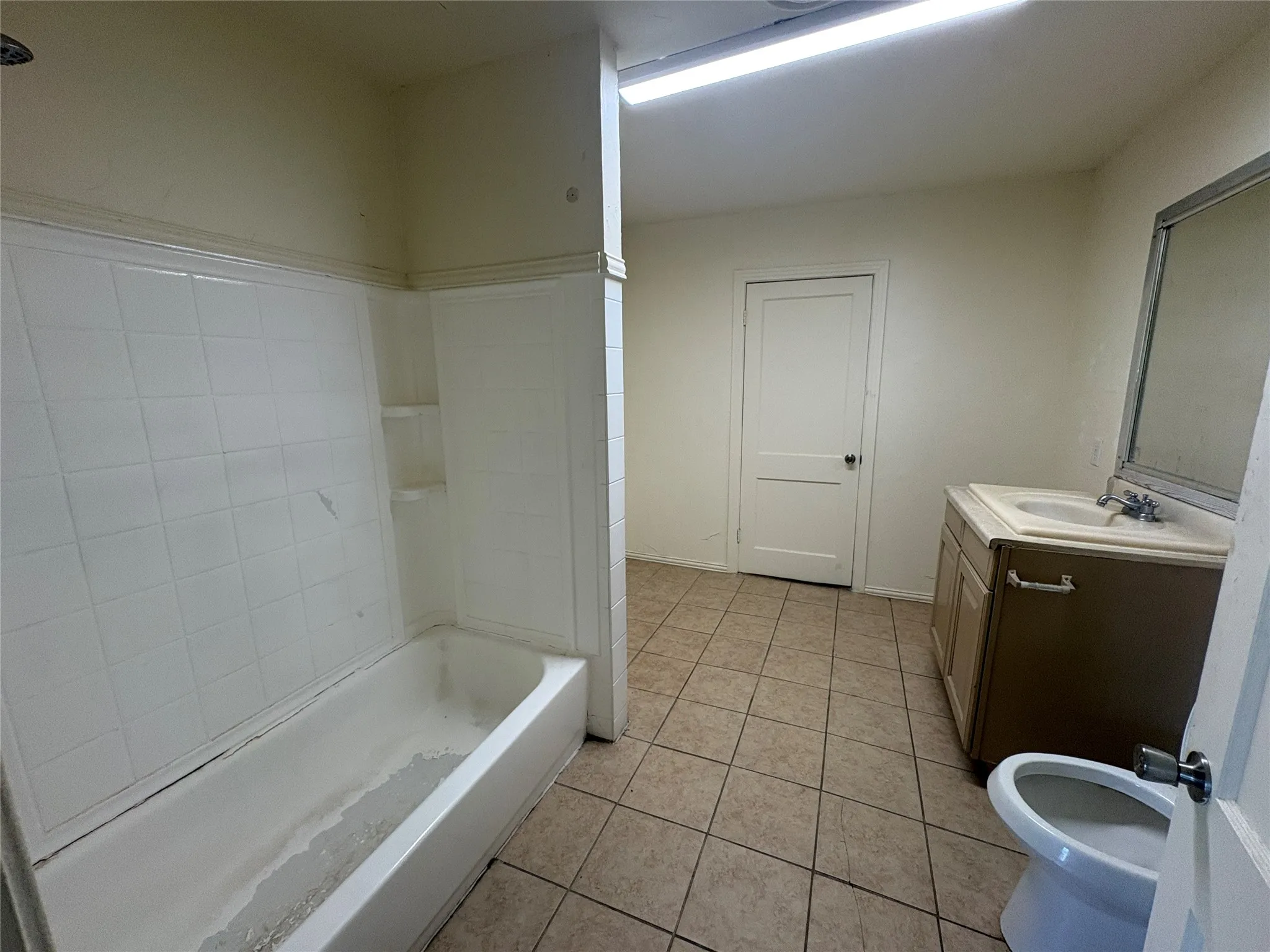 Tile flooring, built-in bathtub with tiled surround, vanity with integrated sink, wall-mounted mirror, and white interior door