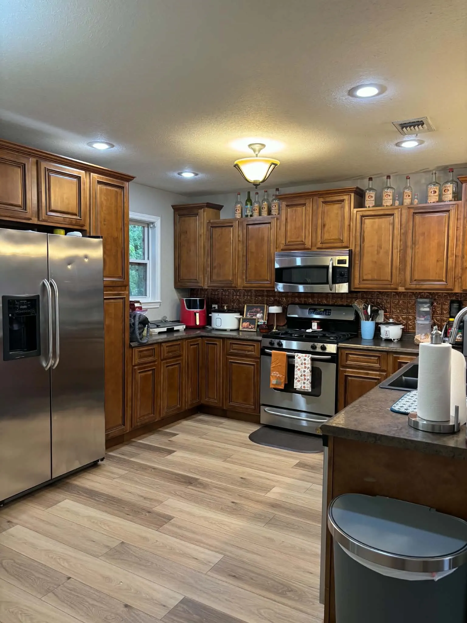 Wood-finish flooring, recessed lighting, stainless steel appliances, wood cabinetry, and a textured backsplash