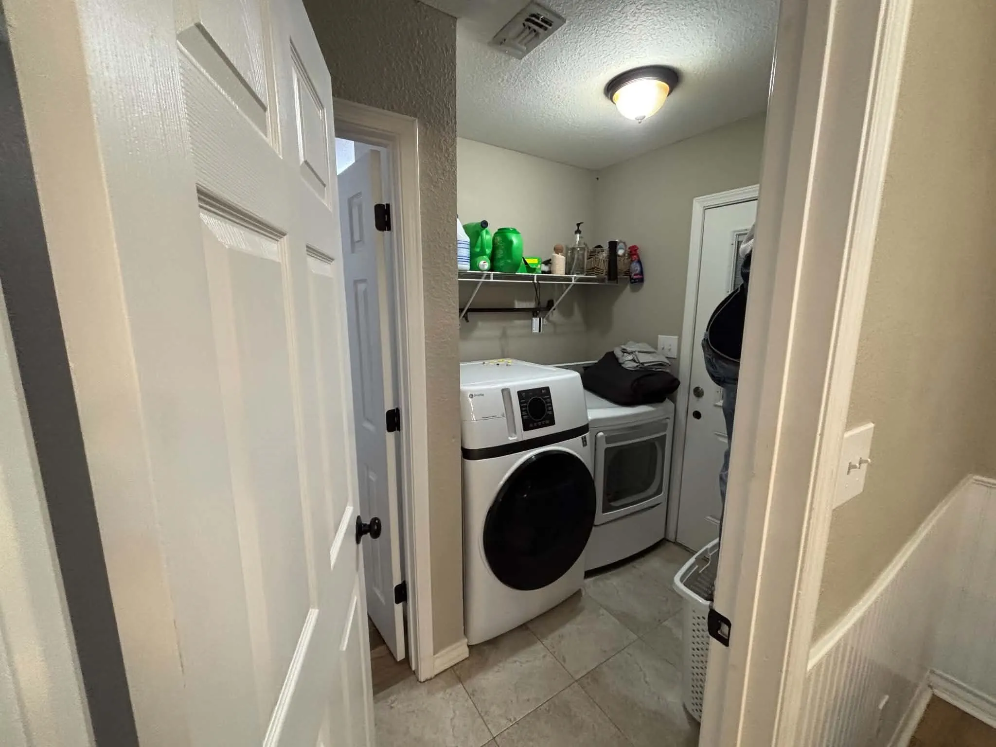 Laundry area featuring tile flooring, wall-mounted shelving, and overhead lighting-washer/dryer not included