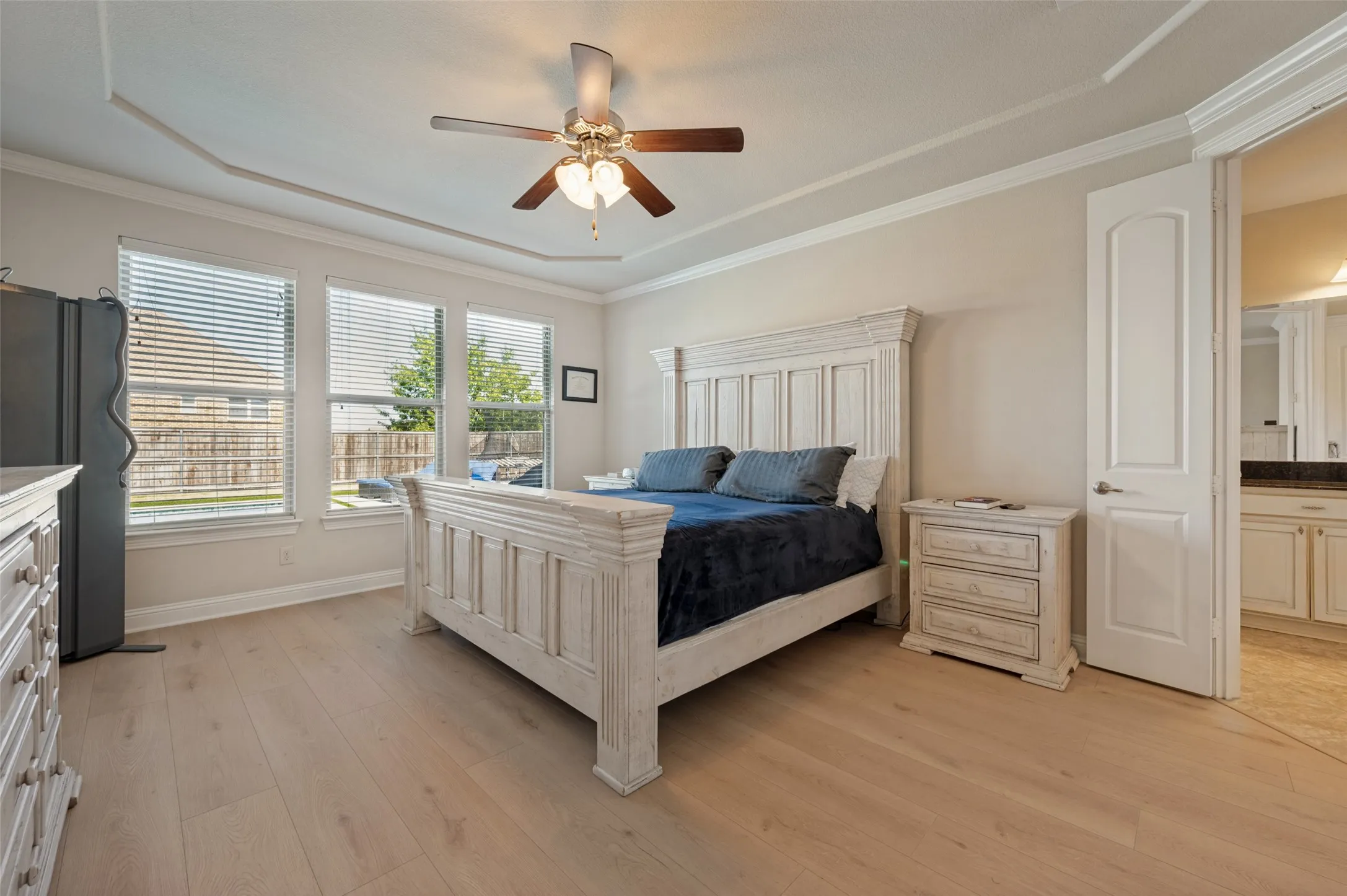 Tray ceiling, crown molding, wood-finish flooring, ceiling fan with light fixture, three large windows