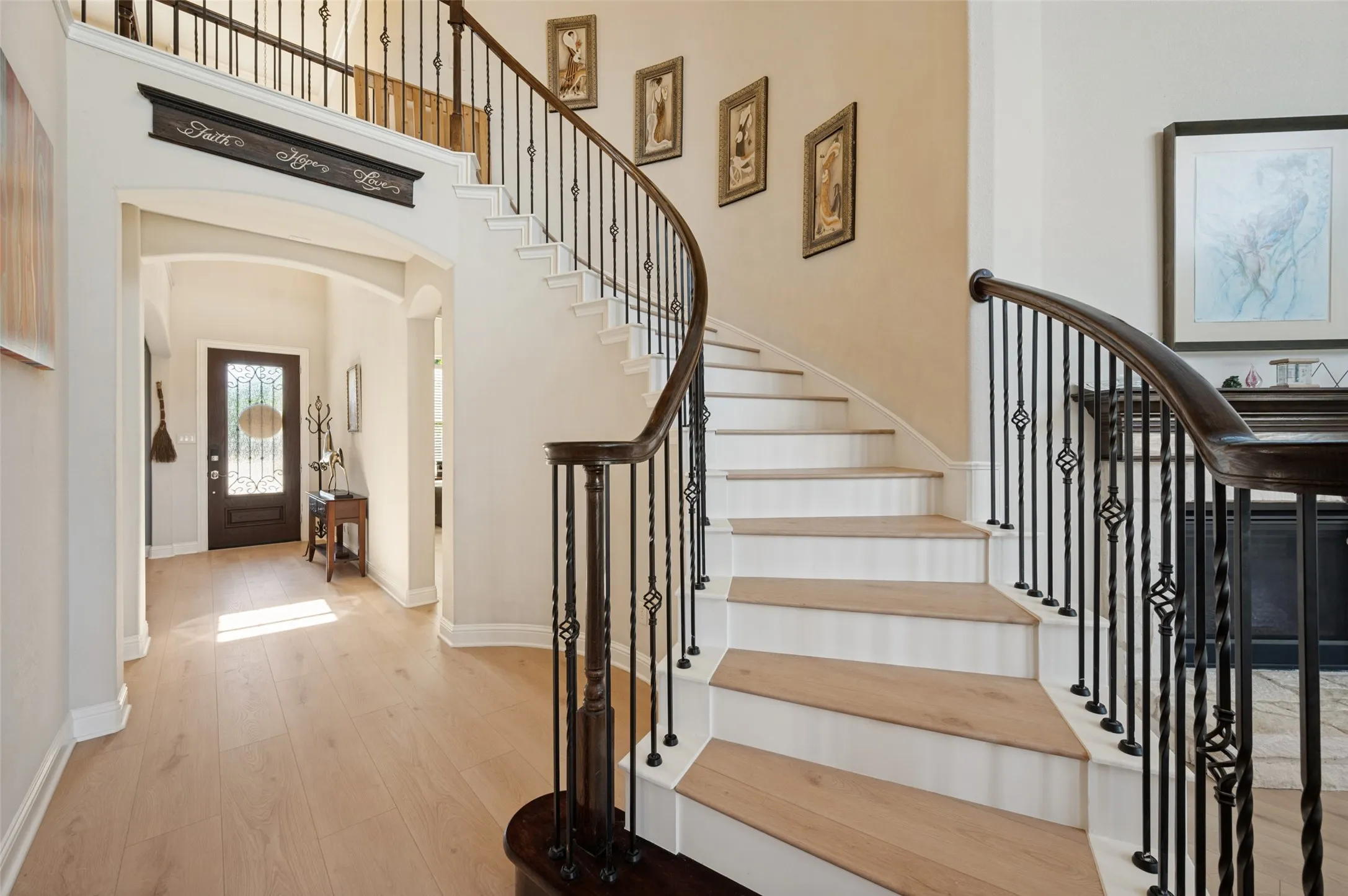 Grand foyer with light wood-finish flooring, a curved staircase featuring dark wood handrails and wrought iron balusters, and arched doorways