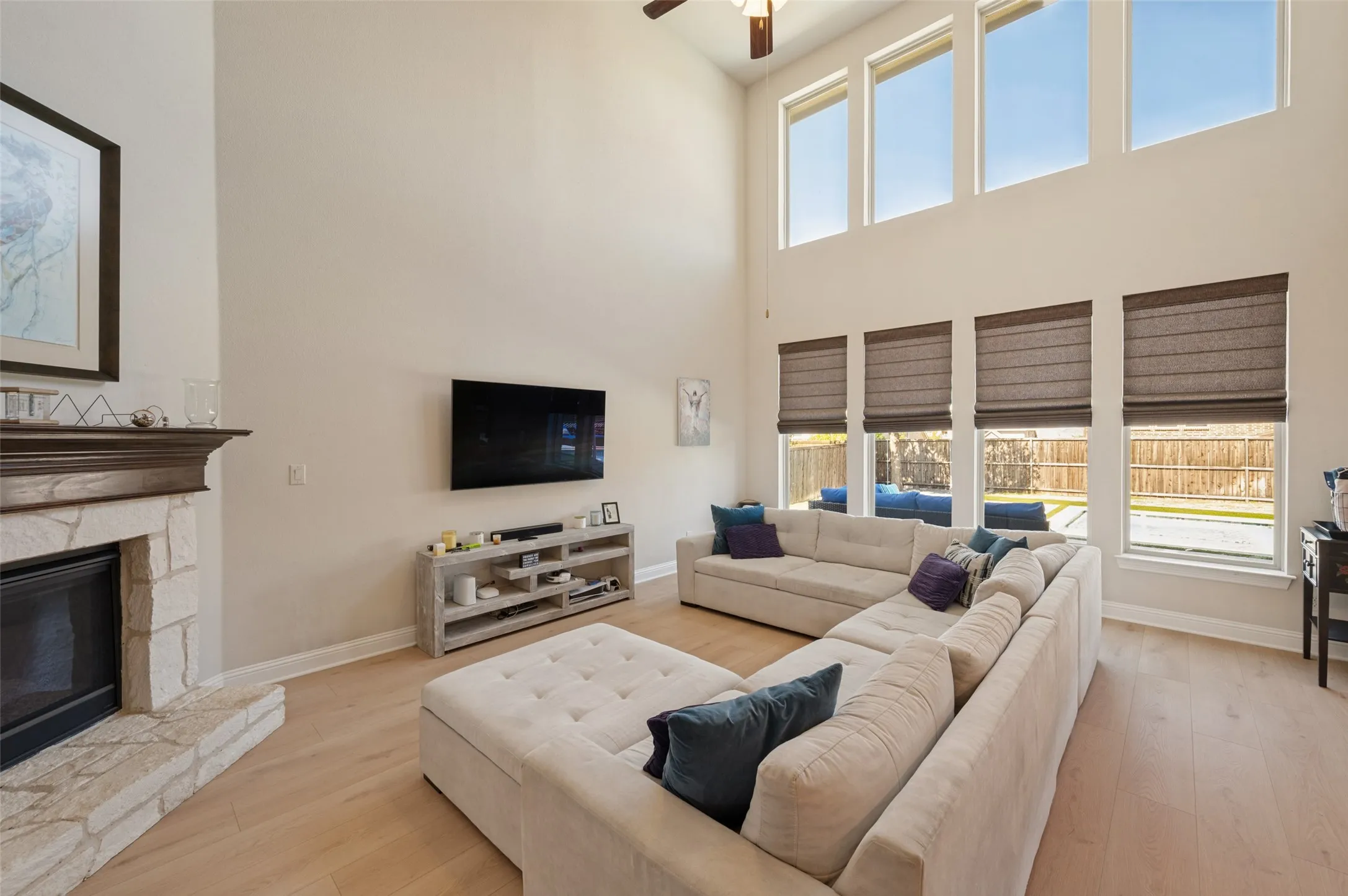 Vaulted ceiling living area featuring a stone fireplace, wood-finish flooring, and multiple large windows with integrated blinds
