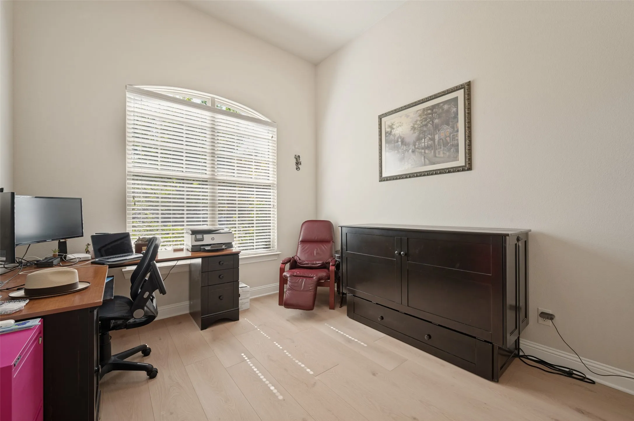 Arched window with horizontal blinds, vaulted ceiling, light wood-finish flooring, and a built-in dark wood cabinet