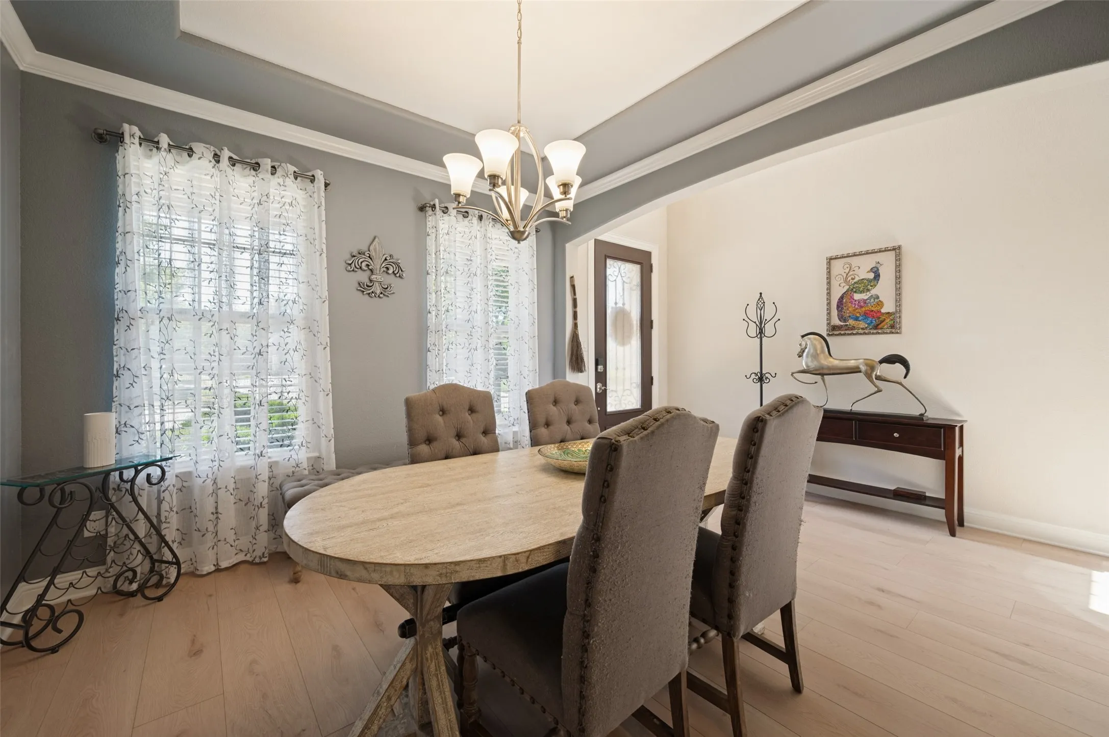 Elegant dining room showcasing a wood-finish oval table, upholstered dining chairs with nailhead detailing, and a contemporary chandelier