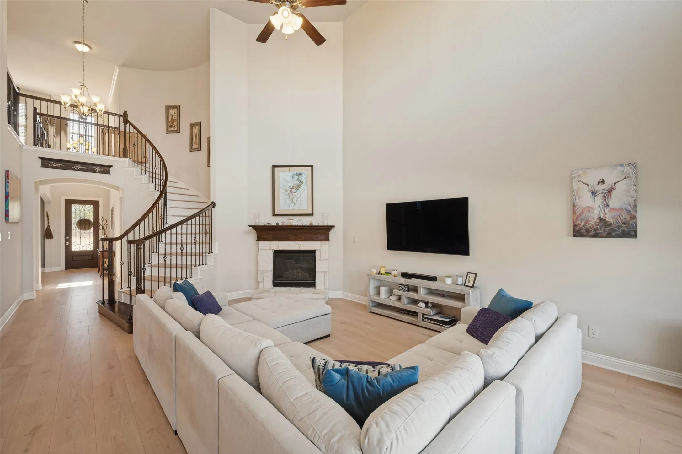 Two-story living area featuring a stone fireplace with wood mantel, a spiral staircase with wrought iron balusters, light wood-finish flooring, and a ceiling fan