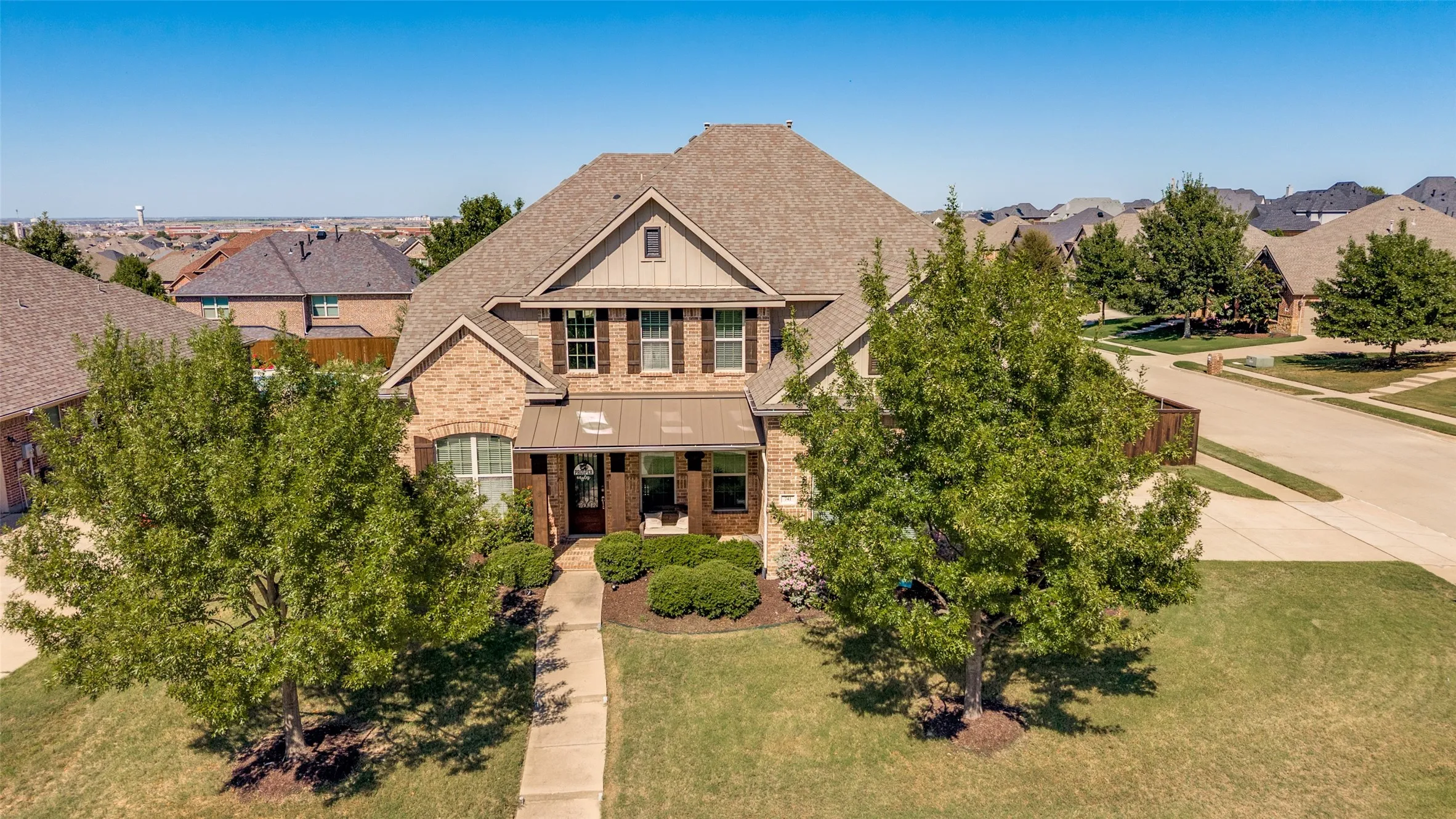 Brick and siding exterior with dark shutters, covered front entry, established landscaping, and an attached garage