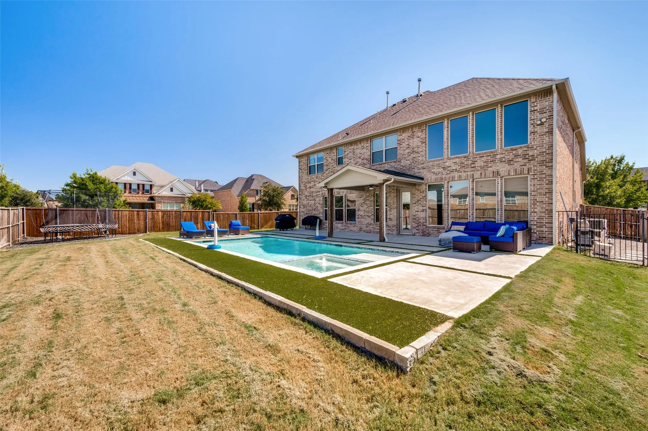 Brick exterior with multiple large windows, covered patio, fenced backyard, inground pool, and integrated spa