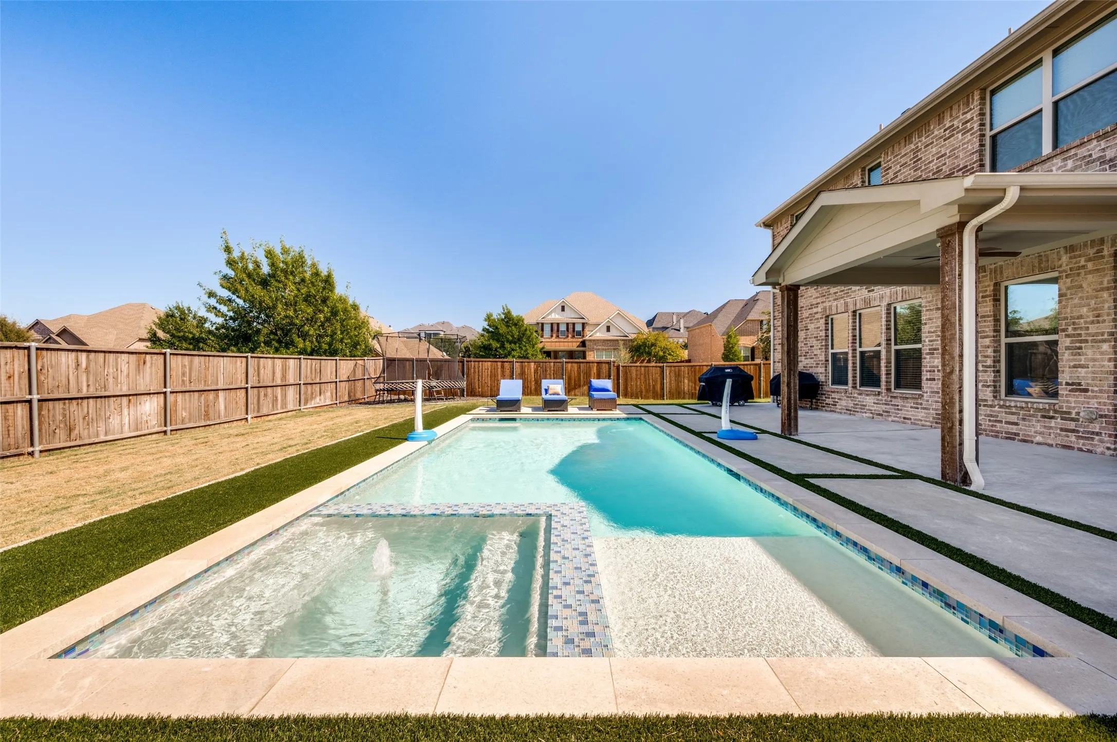 Contemporary swimming pool with integrated spa, concrete patio, covered outdoor living area, and a brick exterior