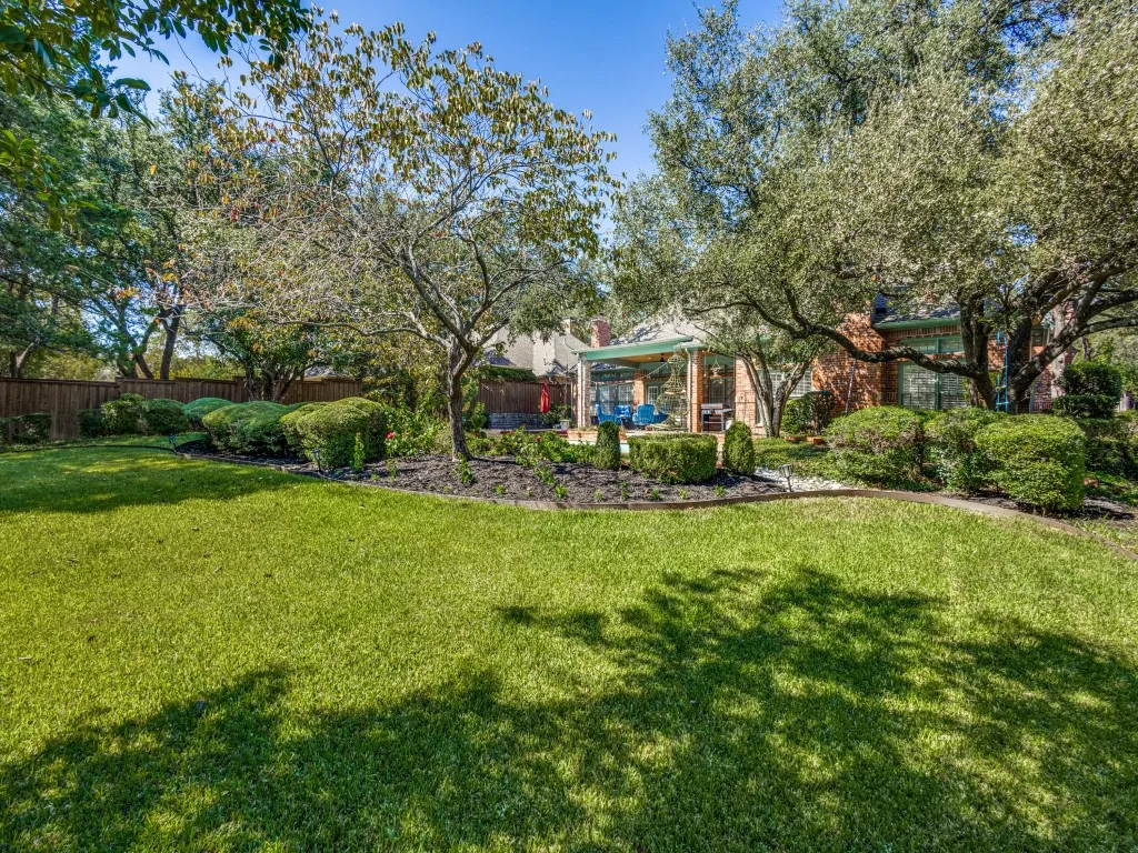 Expansive lawn area, mature trees, manicured hedges, covered patio, wood privacy fencing