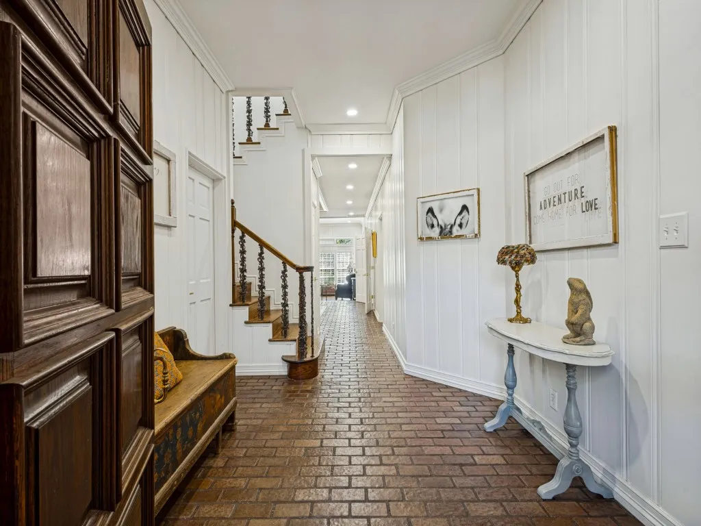 Brick flooring, white vertical paneled walls, crown molding, wood staircase with iron balusters, and recessed lighting