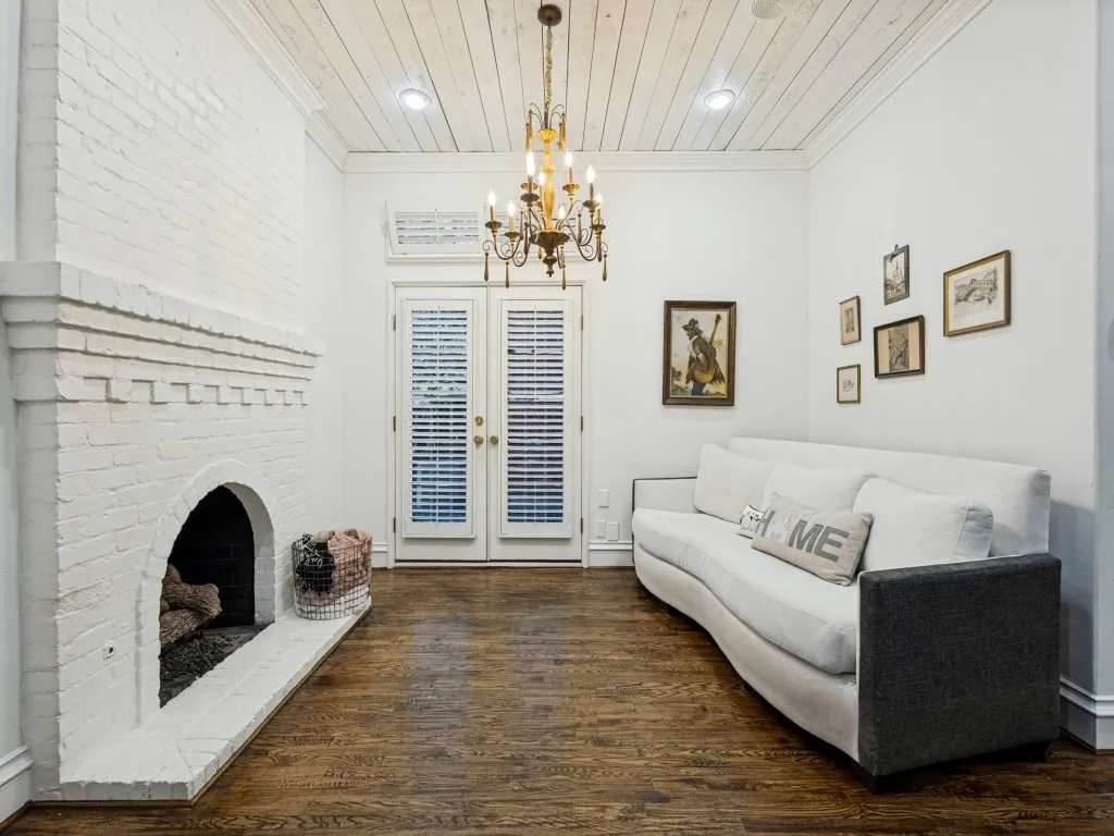 Painted brick fireplace with arched firebox, wood-finish flooring, white planked ceiling, and French doors with louvered inserts