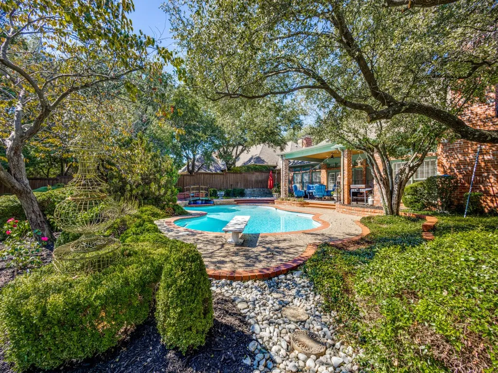 Curved swimming pool with a diving board, brick paver coping, and a covered patio structure
