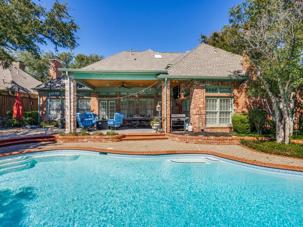 Brick exterior with covered patio, integrated swimming pool with tiled border, and a raised brick patio